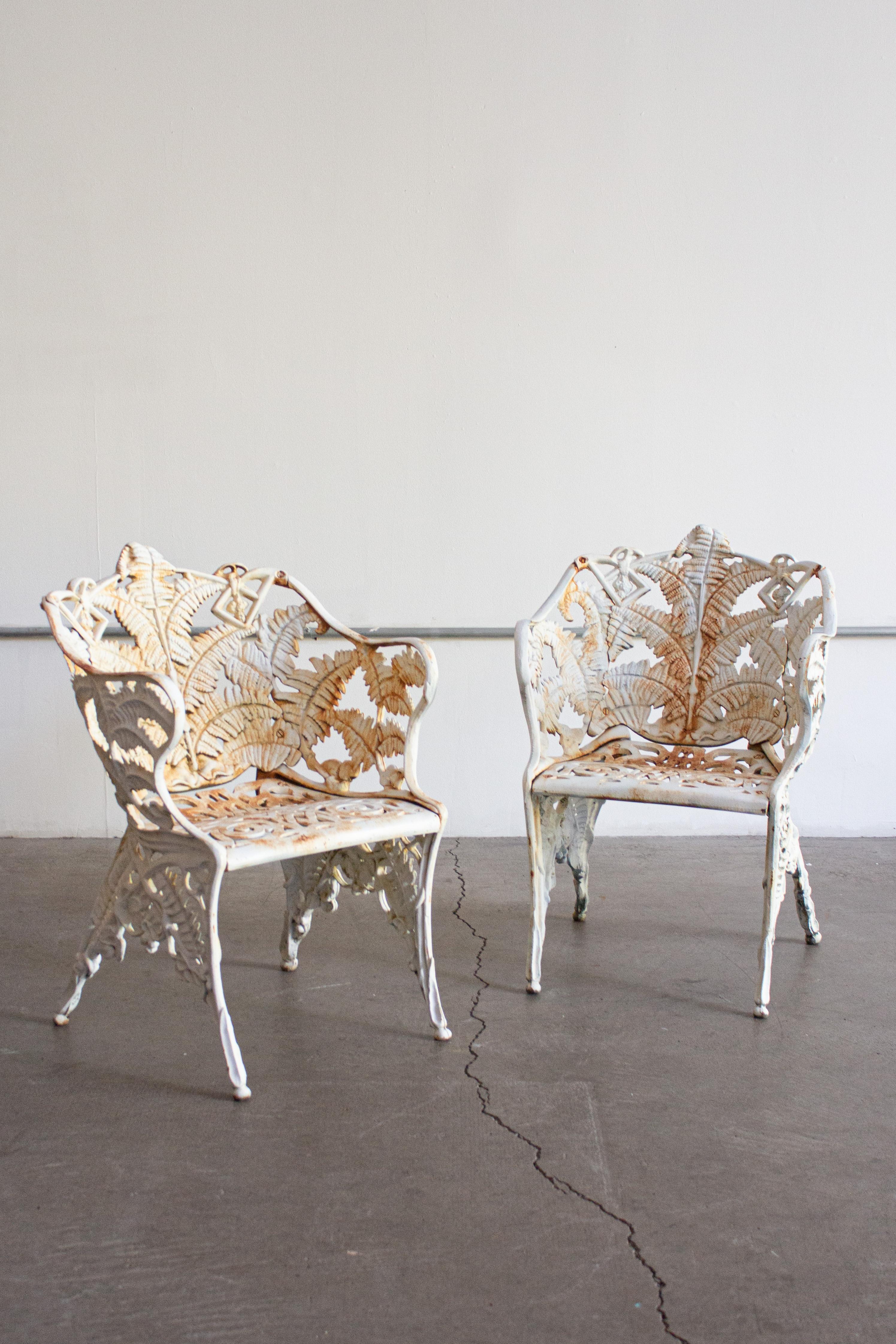 A pair of Victorian cast iron garden chairs in a “Fern” pattern. White paint with areas of rust showing though. Substantial heavy weight. Petite bench also available, sold separately.