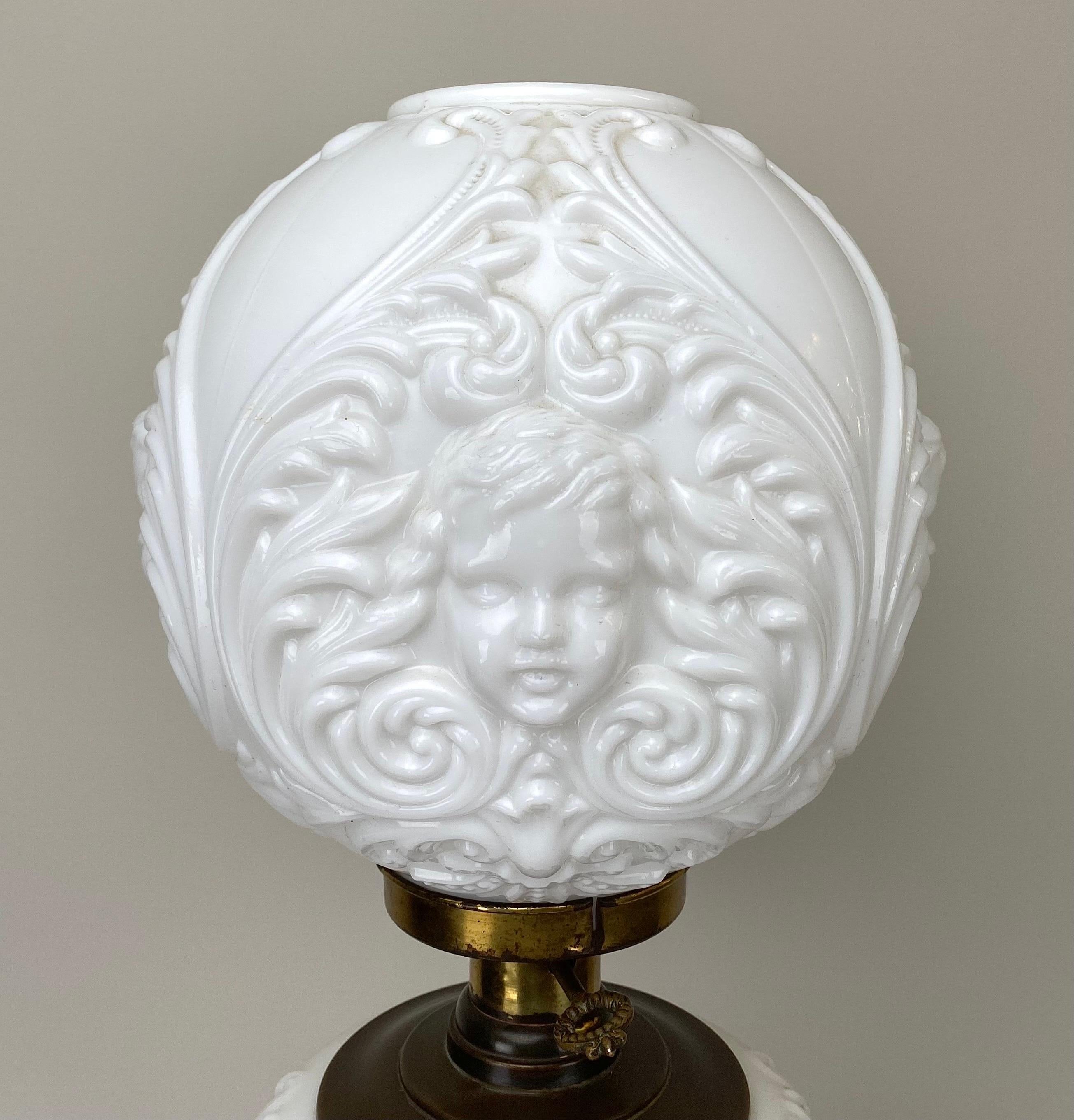  A Victorian style Cherub Face Milk Glass Double Globe Converted Parlor Oil Lamp. This resplendent table lamp is a testament to the opulence of the Victorian era, where ornate details and intricate craftsmanship took center stage. The lamp's frame