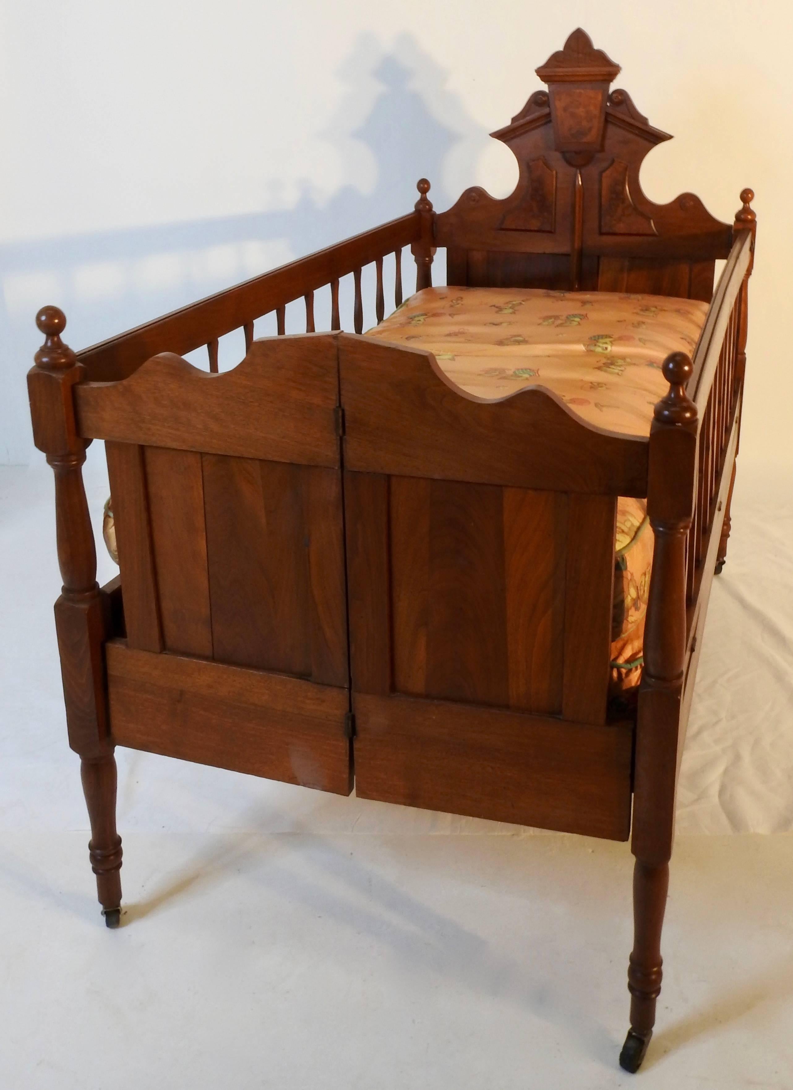 Burled walnut and Classic walnut grace this Victorian baby bed from the 19th century. Includes mattress and springs which is covered in a plastic vinyl type material with stitched seams. The bed sits on four casters rising on a turned wood leg.