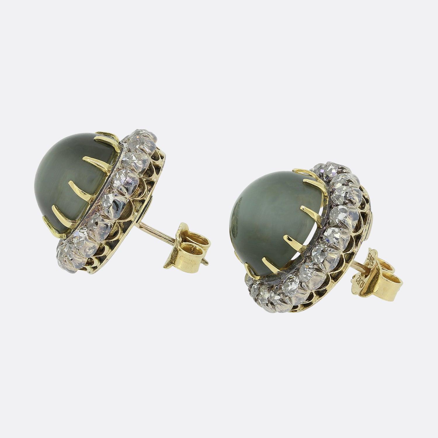 Here we have an antique pair of chrysoberyl and diamond cluster earrings. Crafted during the Victorian era, each piece showcases a large domed chrysoberyl possessing a shimmering honey green colour tone. These iridescent stones are contained within