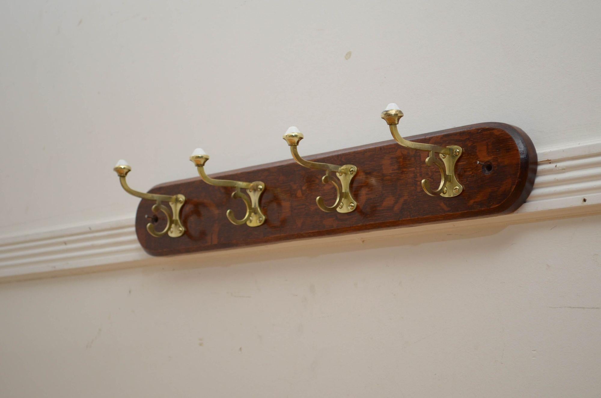 P0274 Elegant Victorian coat rack with four shaped brass and porcelain hooks on solid oak rounded back with chamfered edge and very decorative grain. This antique coat rack has been cleaned and polished and is in home ready condition. c1880
H4.5