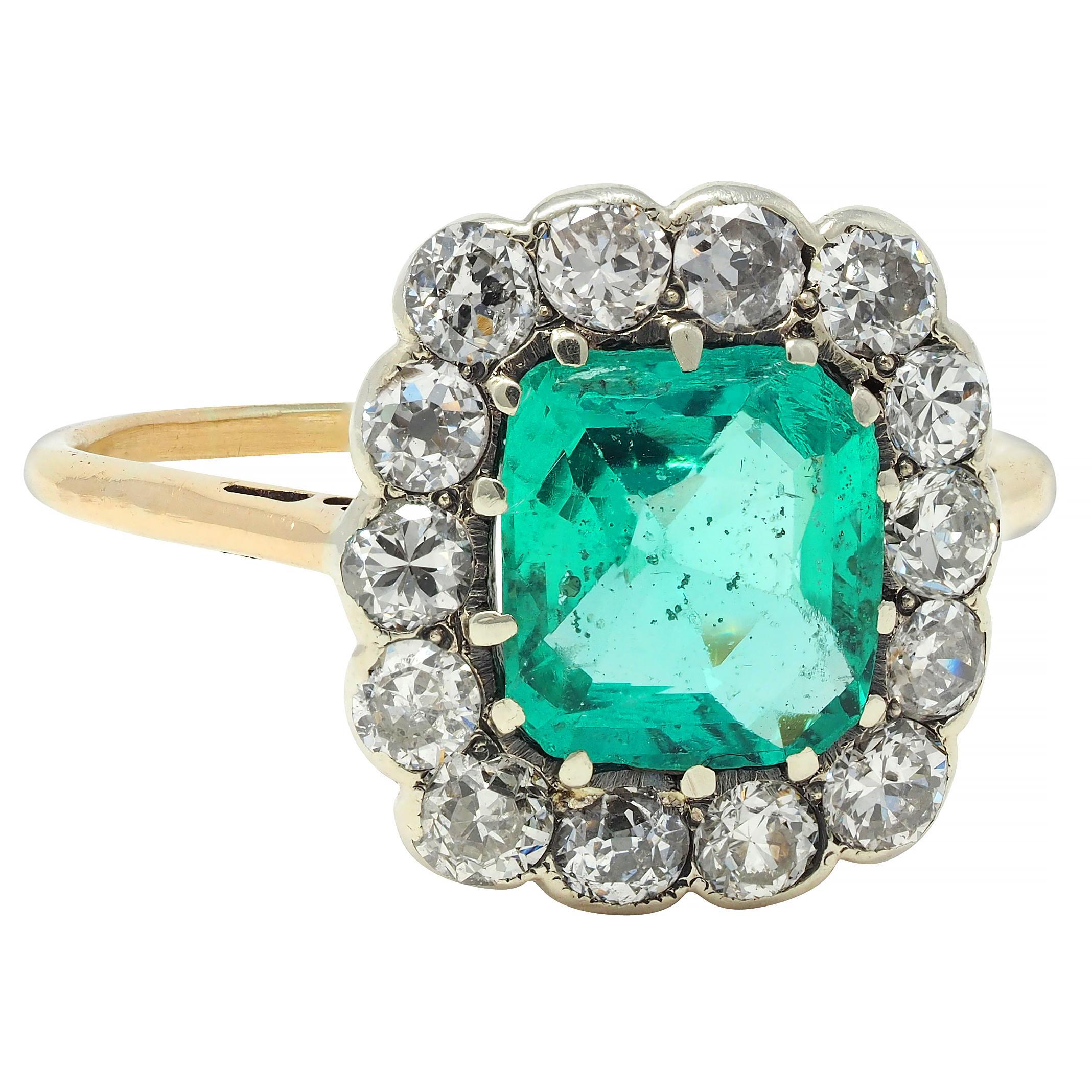 Centering a cushion cut emerald weighing 1.45 carats - transparent green in color 
Natural Colombian in origin with no indications of clarity enhancement 
Prong set in silver-topped head with a halo surround of diamonds
Old European cut and weighing