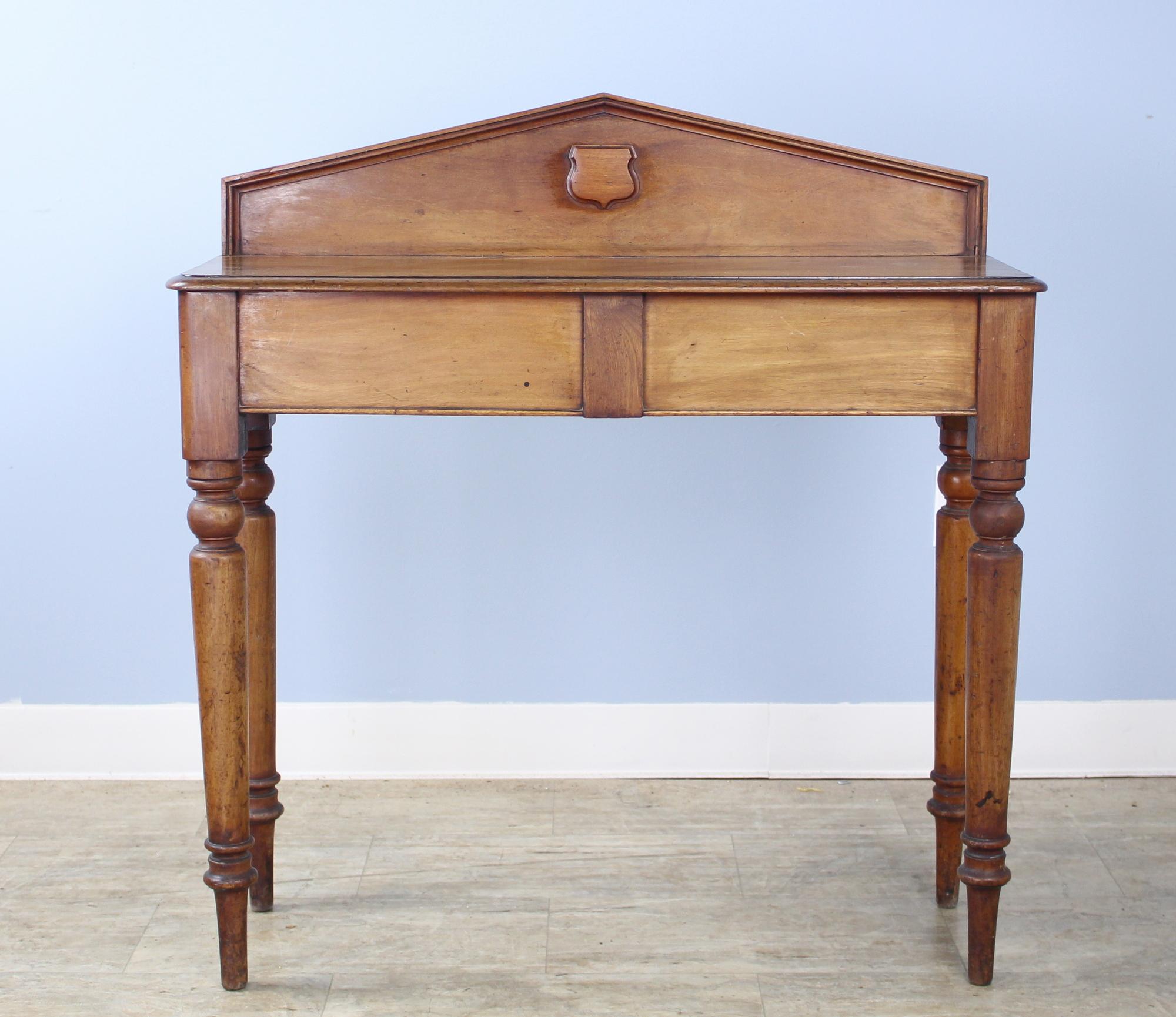 A small Victorian console table in mellow mahogany with a secret compartment on the right side. Pretty turned legs and a galleried back with a decorative medallion. This is the perfect hall piece for lamps and keys, or a good table for behind a love