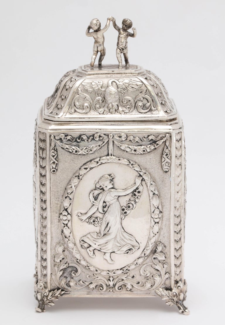Victorian, Continental silver .800, footed tea caddy, Germany, with Hannau marks, circa. 1895, B. Neresheimer and Sohne - makers. Chased with dancing maidens, and having a finial consisting of two children. Measures 6 1/4 inches high to top of