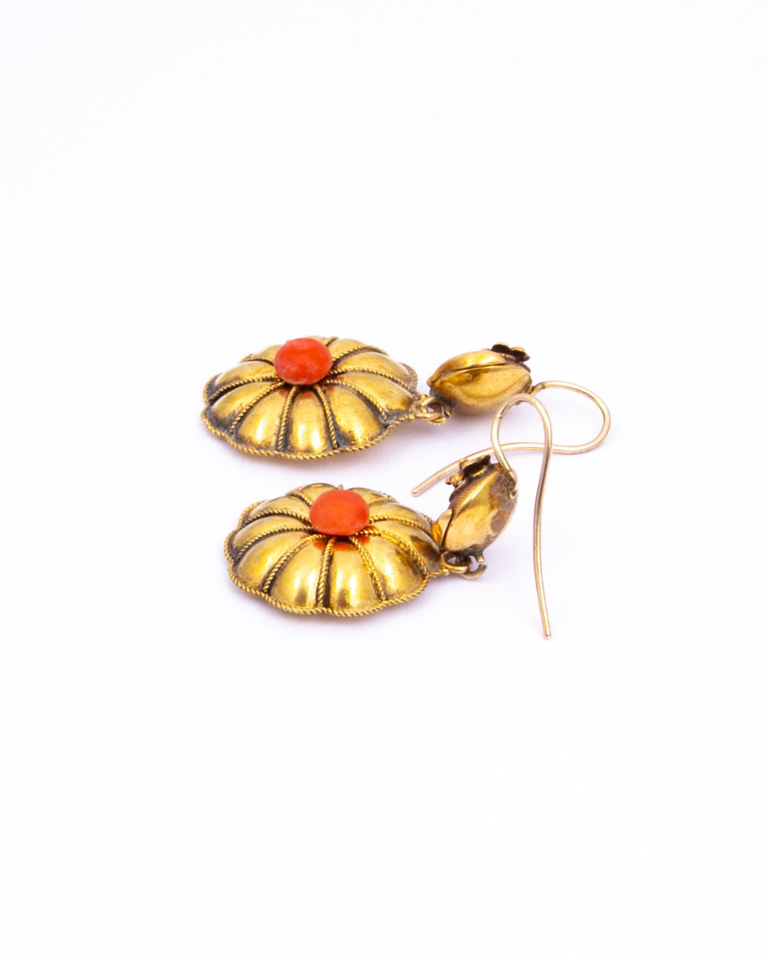These statement earrings are modelled in 18ct gold and have a smooth round piece of coral at the centre if the drops. Above these drops there are fabric like textured circles with a delicate flower wrapped around them. 

Drop From Ear: 41mm 
Bottom