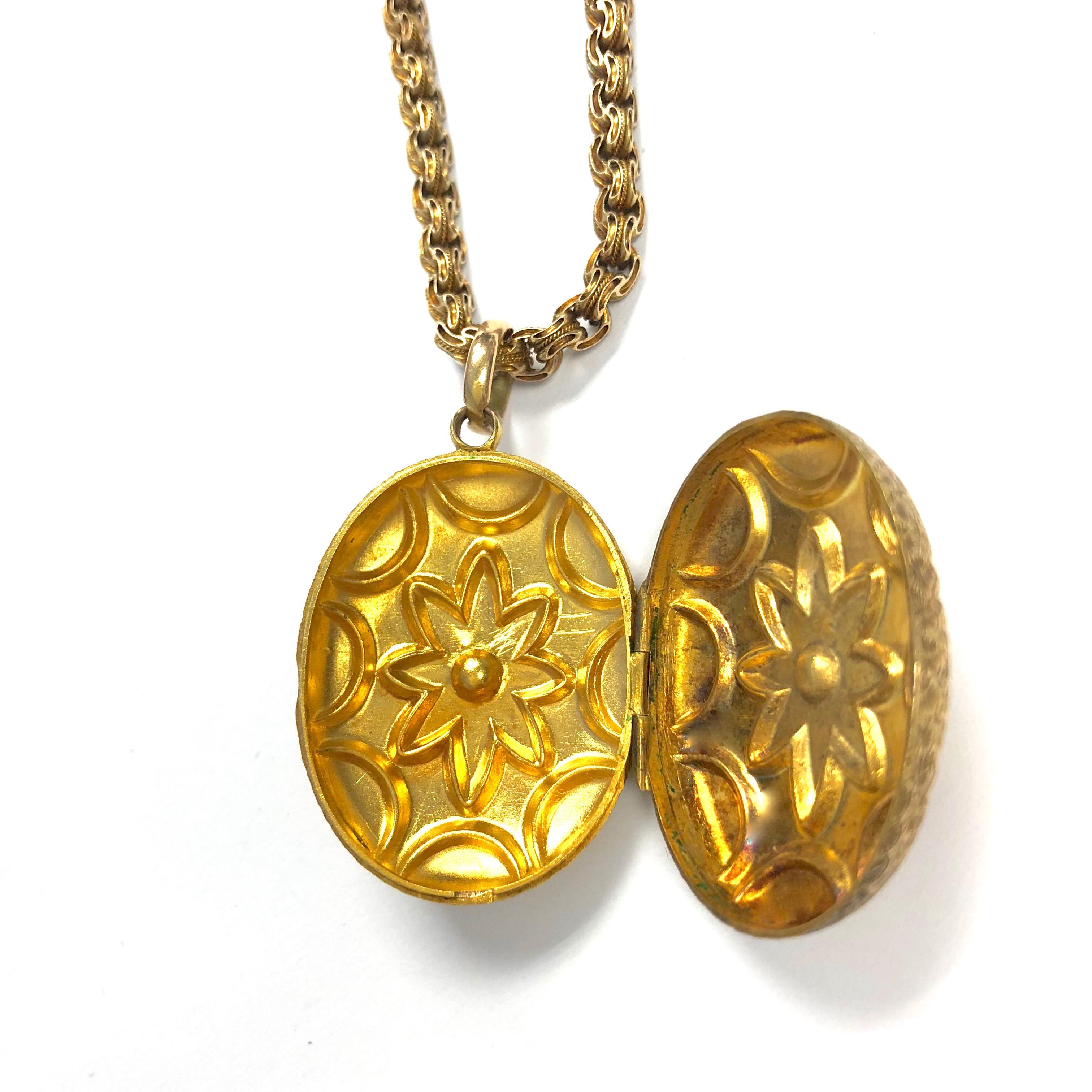 Crafted in 14K yellow gold, the locket features a mirrored design of coral and hand engraving on each side. The pendant is supported by an eighteen inch length antique chain terminating in spring-ring claps. 
Pendant measurements: 1 