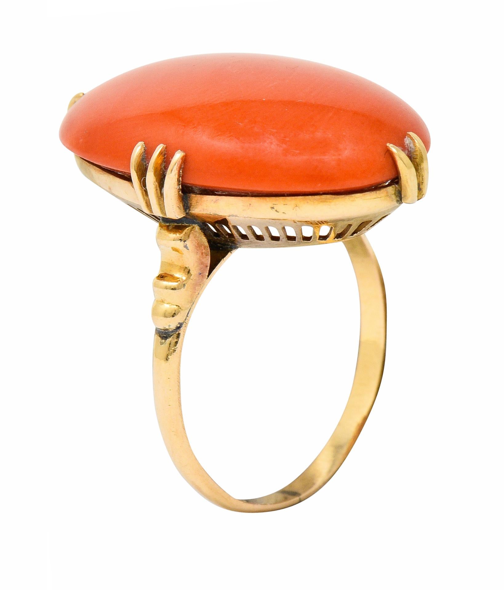 Centering an oval coral cabochon measuring approximately 21.7 x 13.5 mm

Opaque and a saturated reddish-orange color with very even distribution

Set with split prongs and features a pierced striated gallery

Stamped K18 for 18 karat gold

Circa: