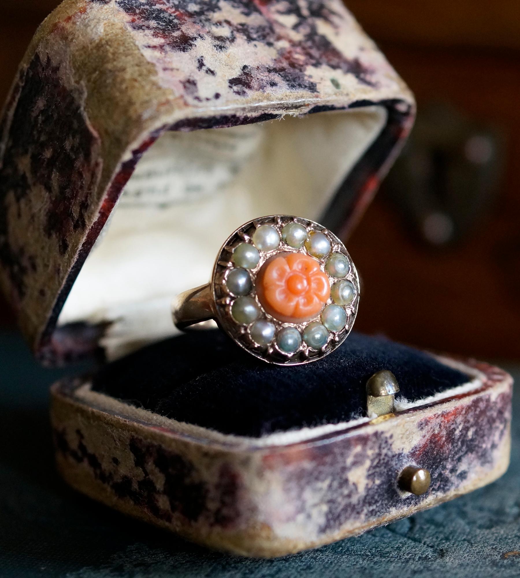 Beautiful and bold low profile Victorian cluster dress ring, featuring 12 seed pearls surrounding a central orange coral stone carved in a floral motif, and cast in 9ct gold. 

Coral was hugely popular in Victorian jewellery, and considered a lucky