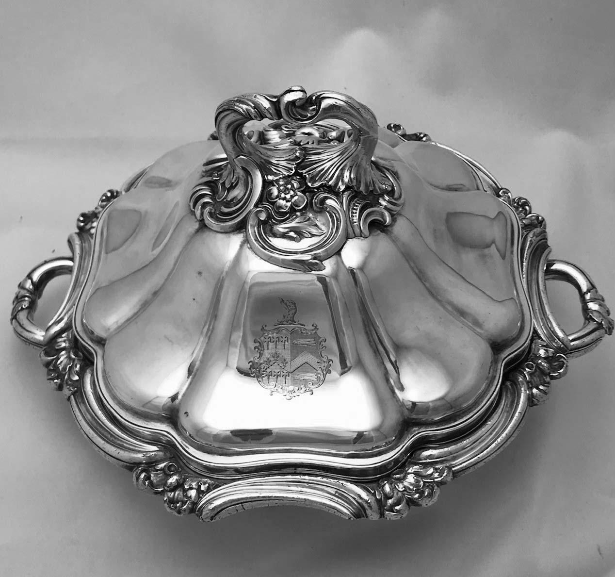 This is a wonderful example of the form. Two-handled, within sinuous border and raised on bun feet, the base is fitted with a water compartment complete with original silver plated stopper. The cover is lobed rising to a boldly moulded leafy handle.
