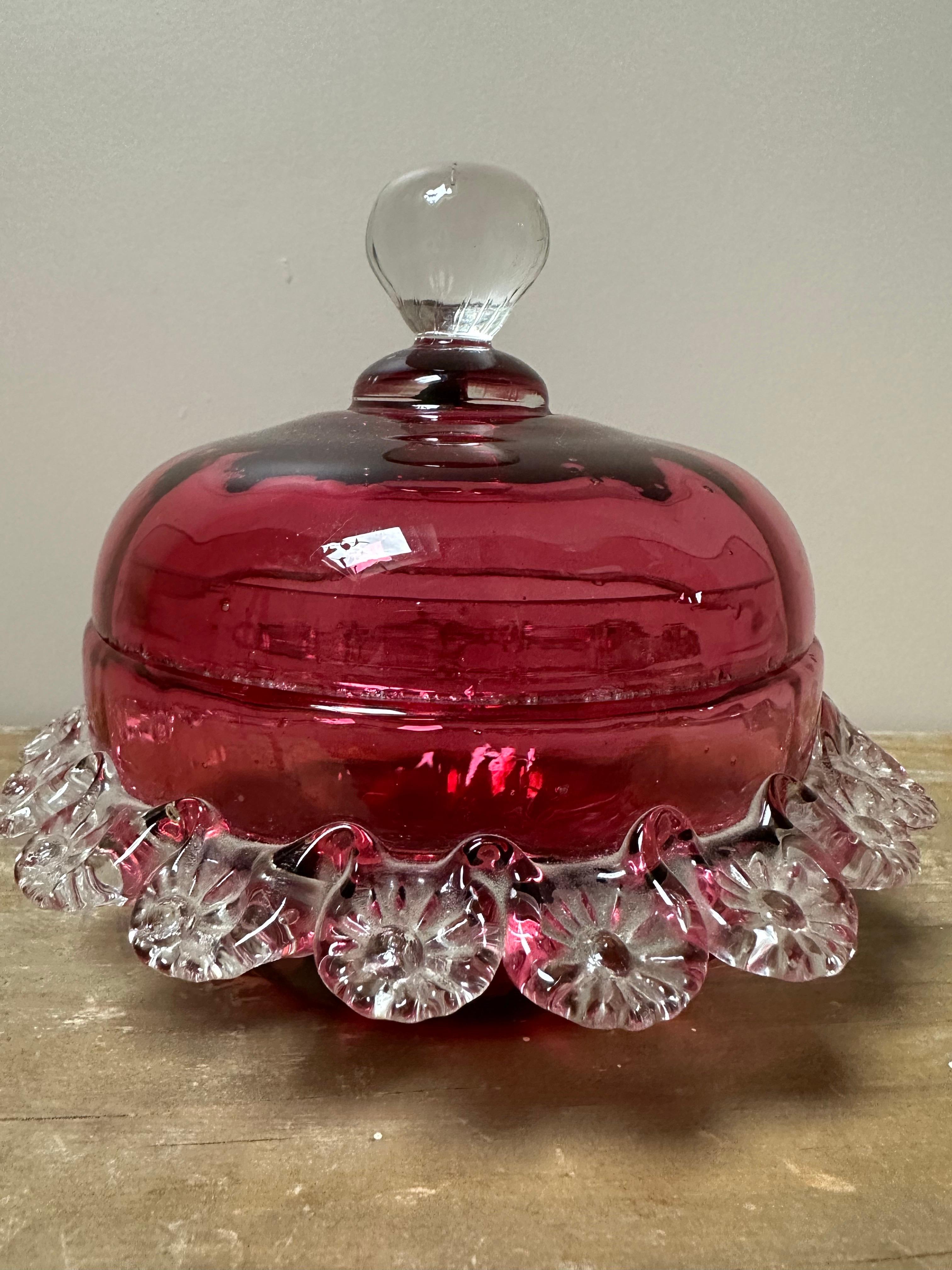 Il s'agit d'un ancien plat à couvercle en verre de canneberge. Il s'agit d'un type de verrerie décorative connue pour sa couleur rose ou rouge distinctive, qui est créée en ajoutant du chlorure d'or au verre en fusion. 
Le plat est orné d'un fleuron