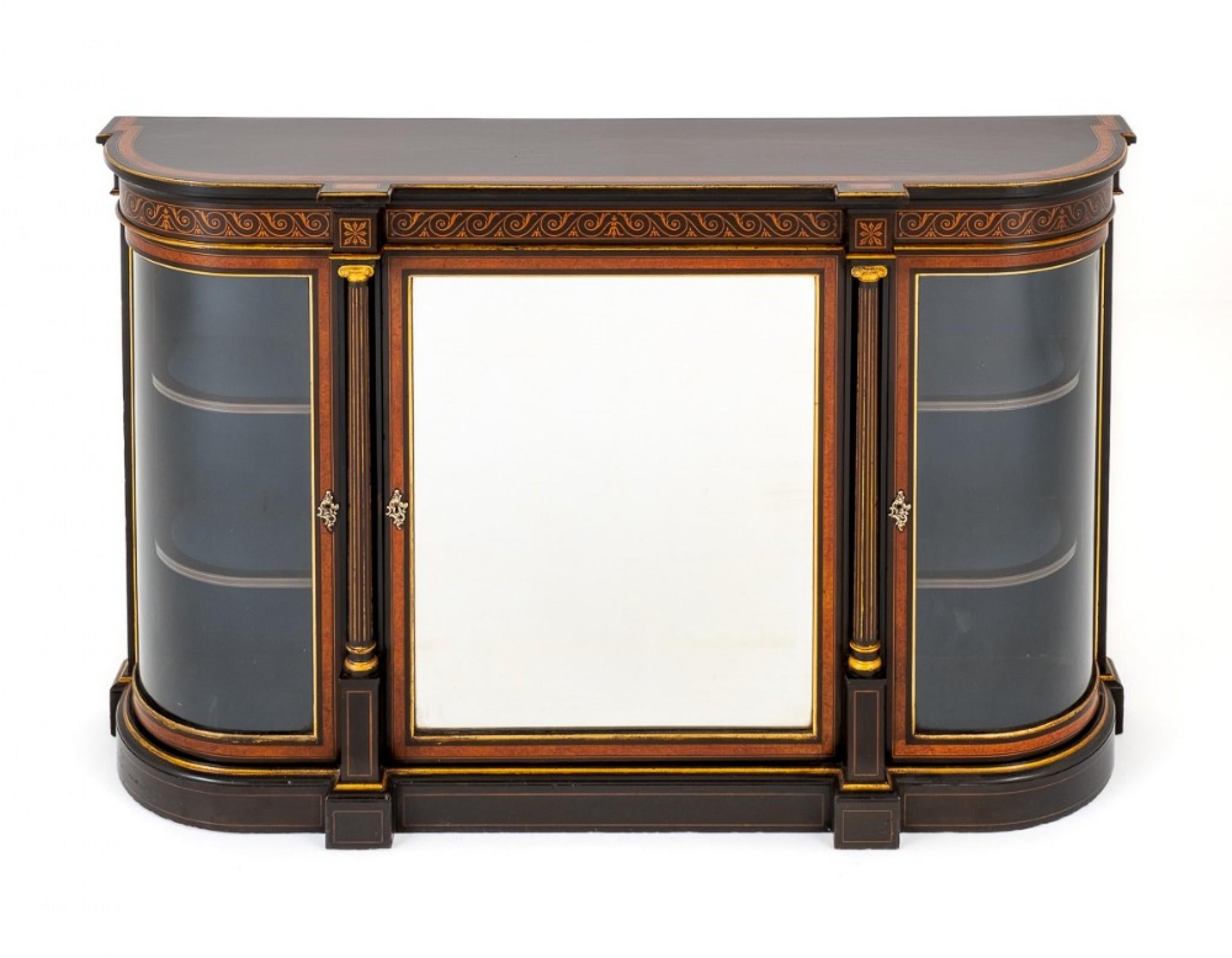 This Victorian ebonised and walnut credenza stands upon a plinth base.
circa 1860
Featuring a mirrored central door flanked by turned and fluted columns.
Either side of the central door we have bowed display cabinets.
The frieze of the cabinet