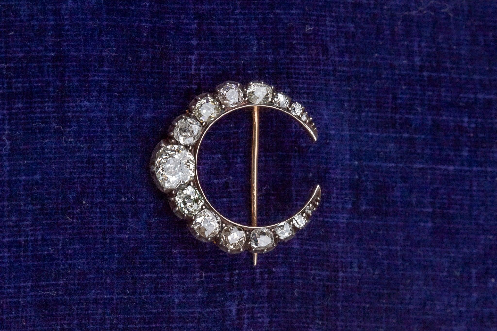 This enchanting Victorian crescent moon brooch, circa 1890, showcases approximately 2.5 carats of old cushion-cut diamonds, each set in crimped silver collet mounts against a warm gold backing. The open gallery design allows light to pass through