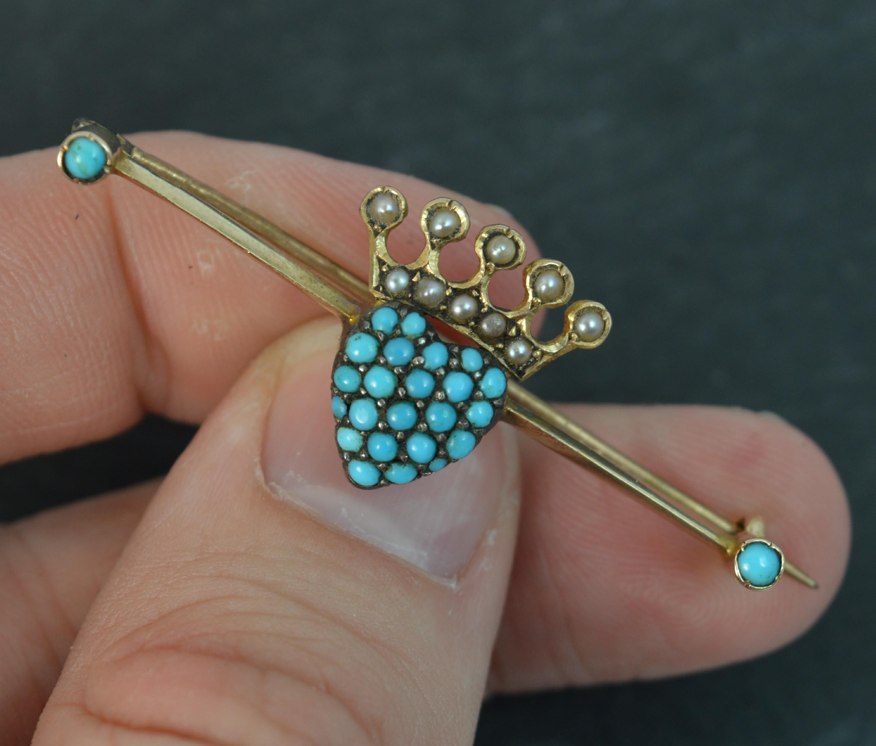A true Victorian period bar brooch. Marked 15ct for 15 carat yellow gold. Designed with a turquoise pave set heart to centre with pearl set crown above and a further turquoise to each end. 43mm long. 15mm x 16mm head approx. 4.0 grams


Condition ;