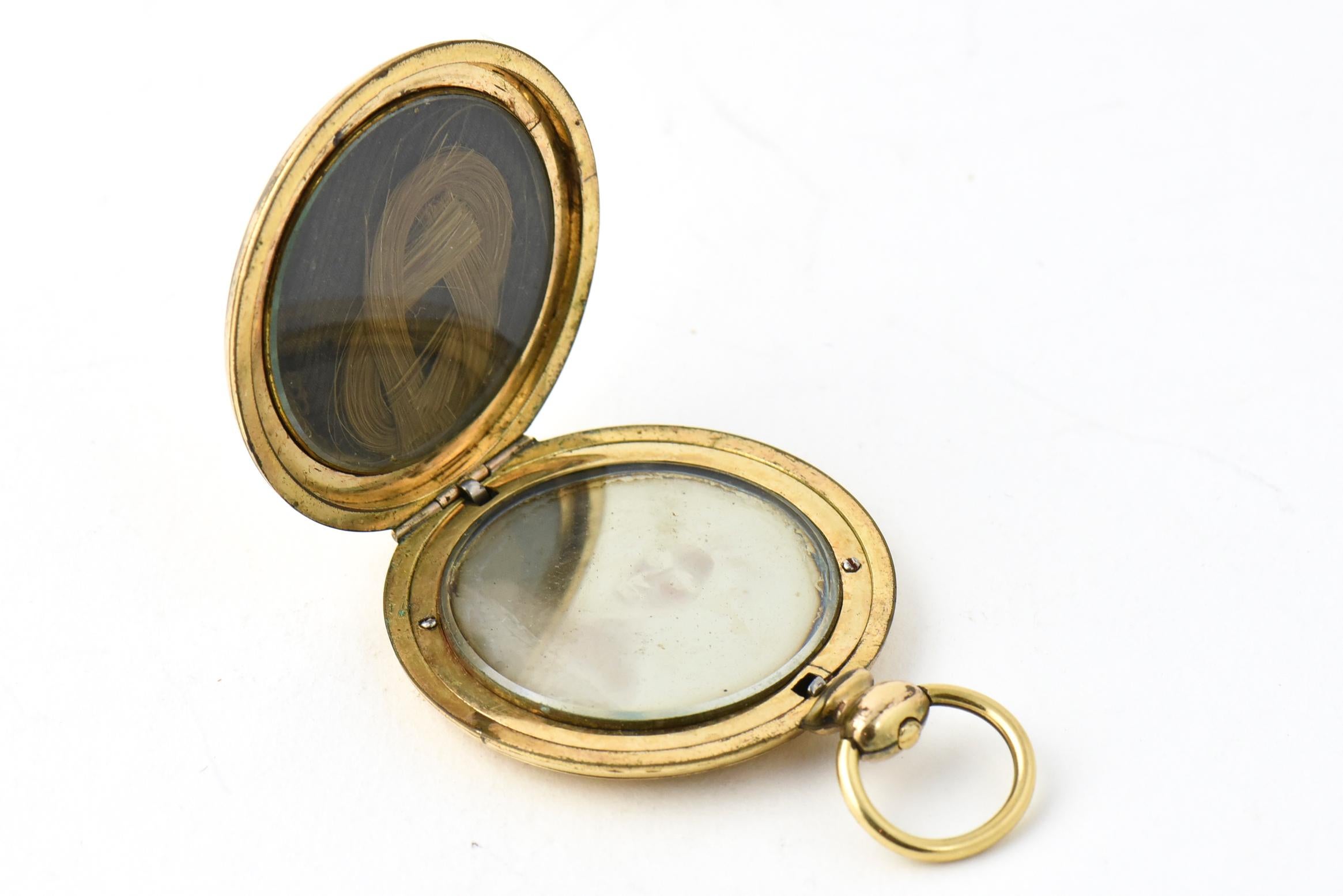Victorian gold-filled memorial locket featuring a daguerreotype portrait of a woman on one side and a lock of hair on the other, both under glass. The exterior has an engine-turned gold finish with a shield and initials 