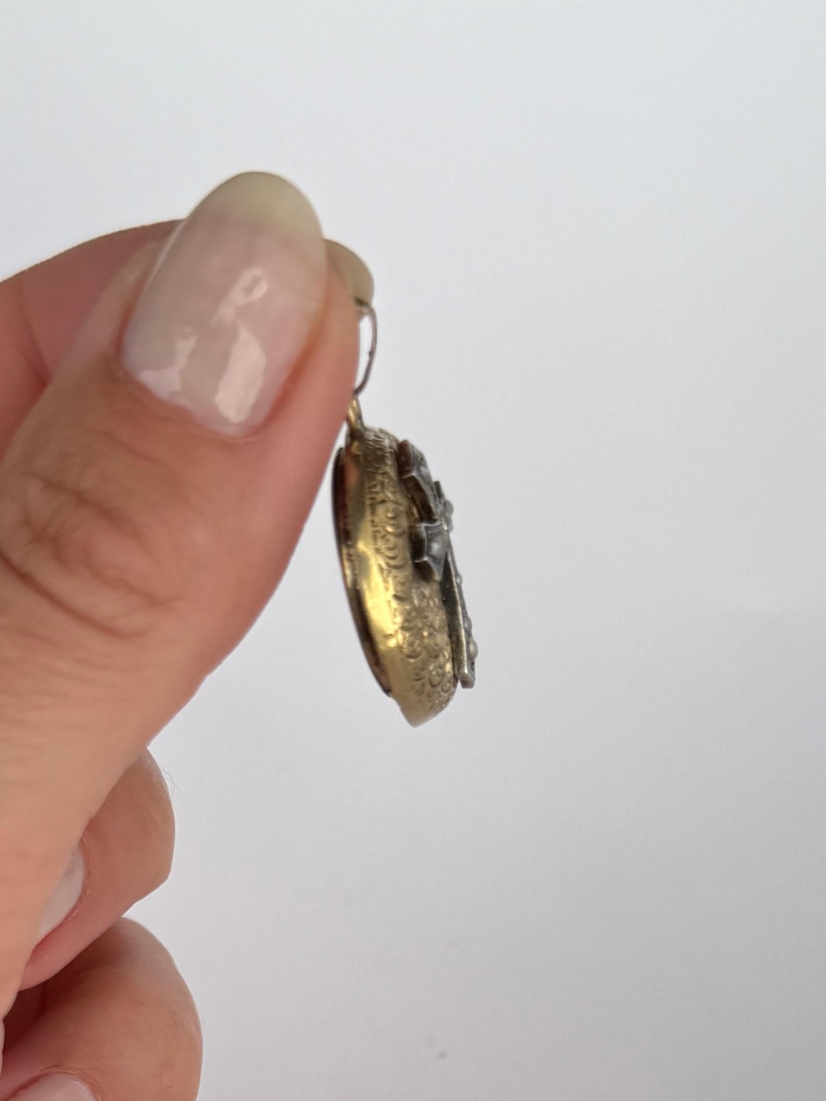 Ce magnifique médaillon est modelé en or jaune brillant 9 carats et présente de fabuleux détails gravés. Le devant du médaillon est orné d'une croix sertie d'un diamant, de perles de rocaille et de détails en émail. Le dos du médaillon contient le