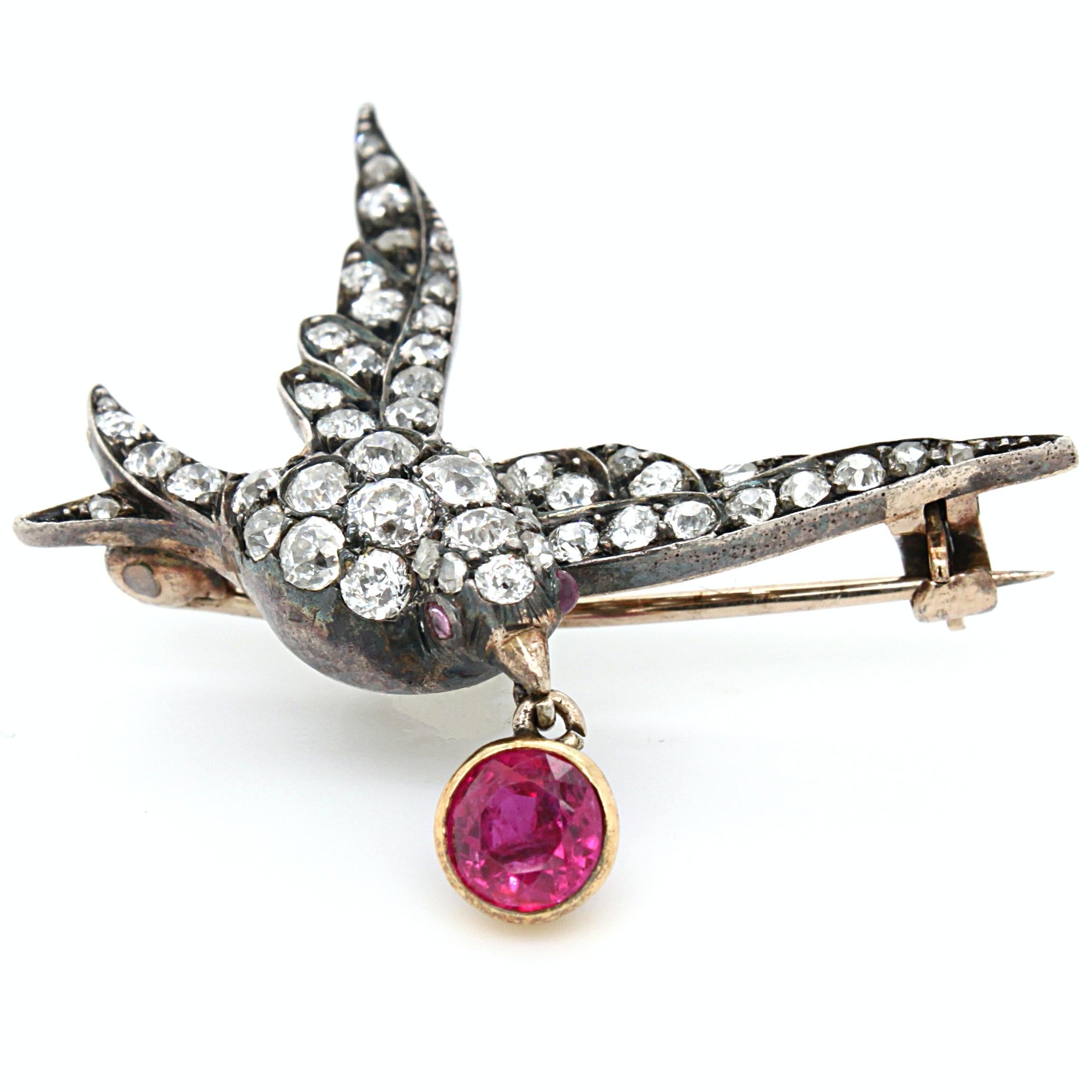 A beautiful diamond and ruby dove brooch, Victorian, ca. 1880s. The dove bird body is set with old cut diamonds of very fine quality, with the eyes set with ruby cabochons. From its beak hangs a facetted round shaped natural, not heated, ruby of