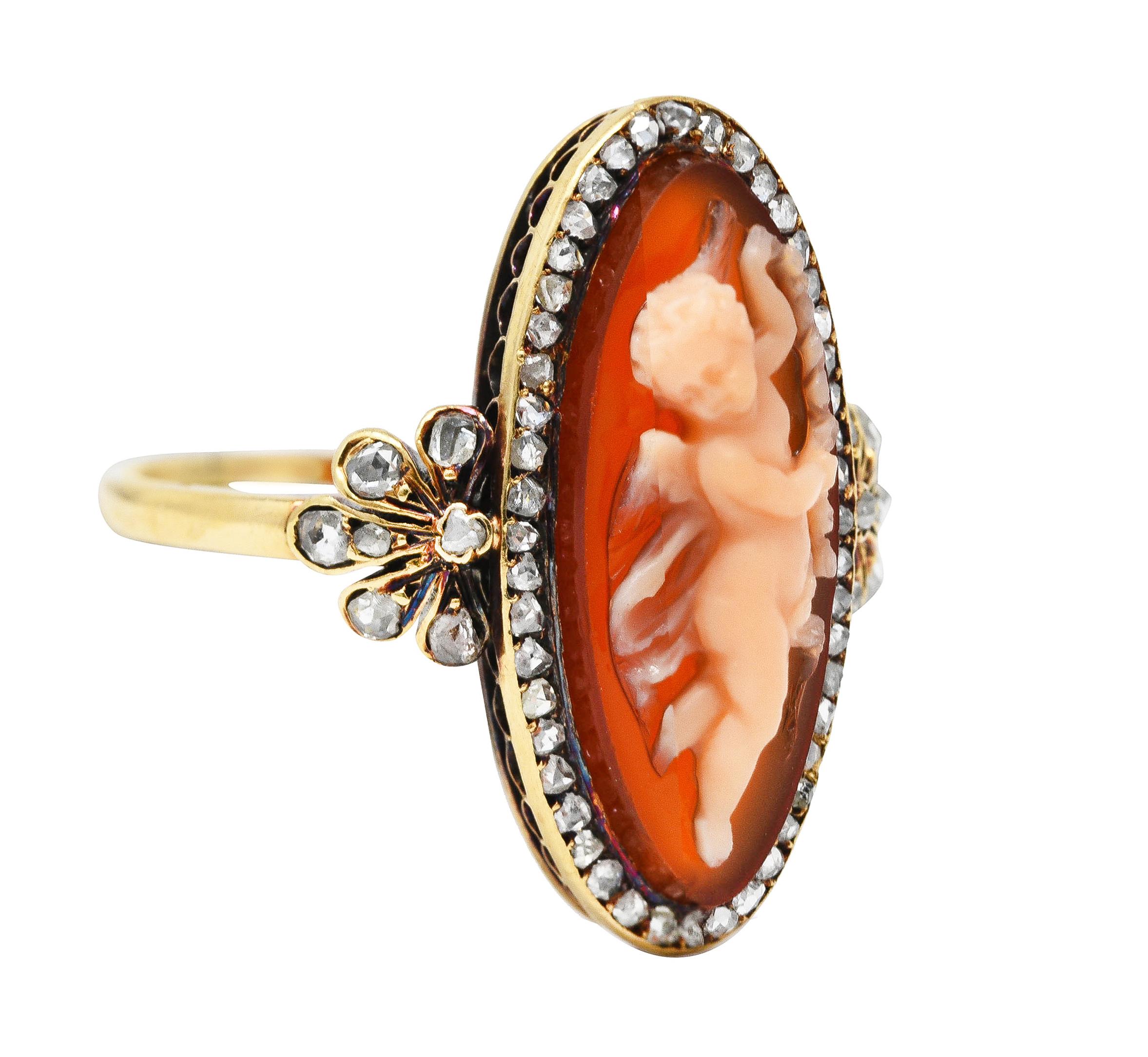 Centering an oval shaped tablet of carnelian carved to depict a winged Cupid holding a garland. Bezel set with a halo surround and foliate shoulder of bead set rose cut diamonds. Weighing approximately 0.72 carat total - quality consistent with cut