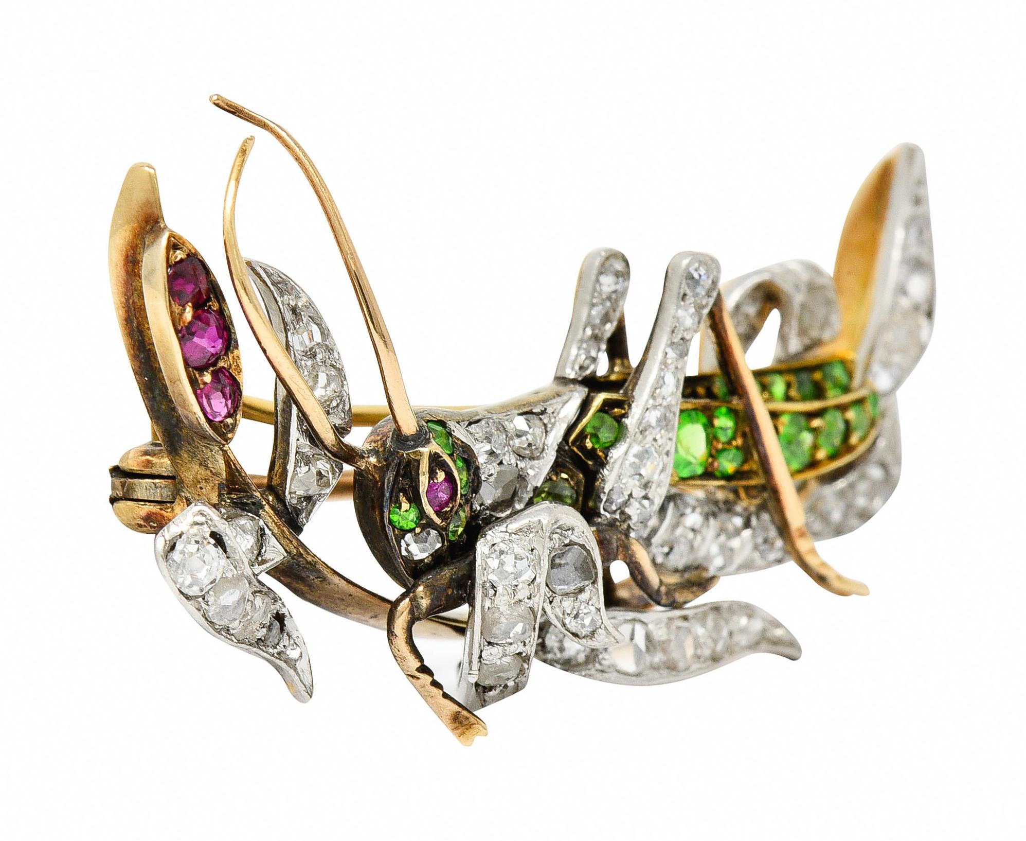 Brooch is designed as a grasshopper with scrolling tendrils and a cattail motif

Cattail and grasshopper's eye are accented by round cut rubies - medium dark purplish red

Grasshopper is accented by round cut demantoid garnets - bright lime