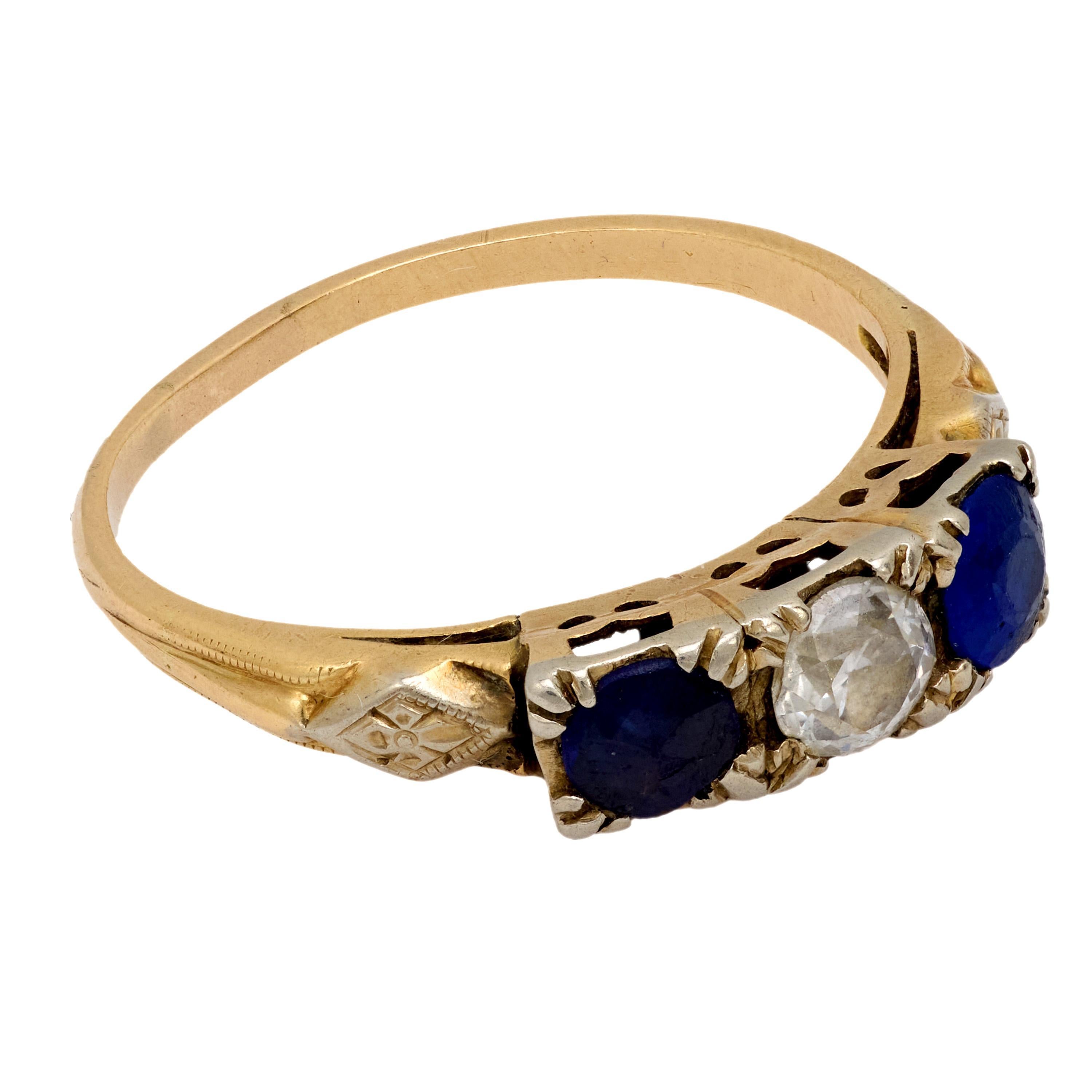 This antique two-tone ring showcases a charming 0.40 carat old European diamond flanked by deep blue sapphires, offering refined Victorian-era elegance and grace.
