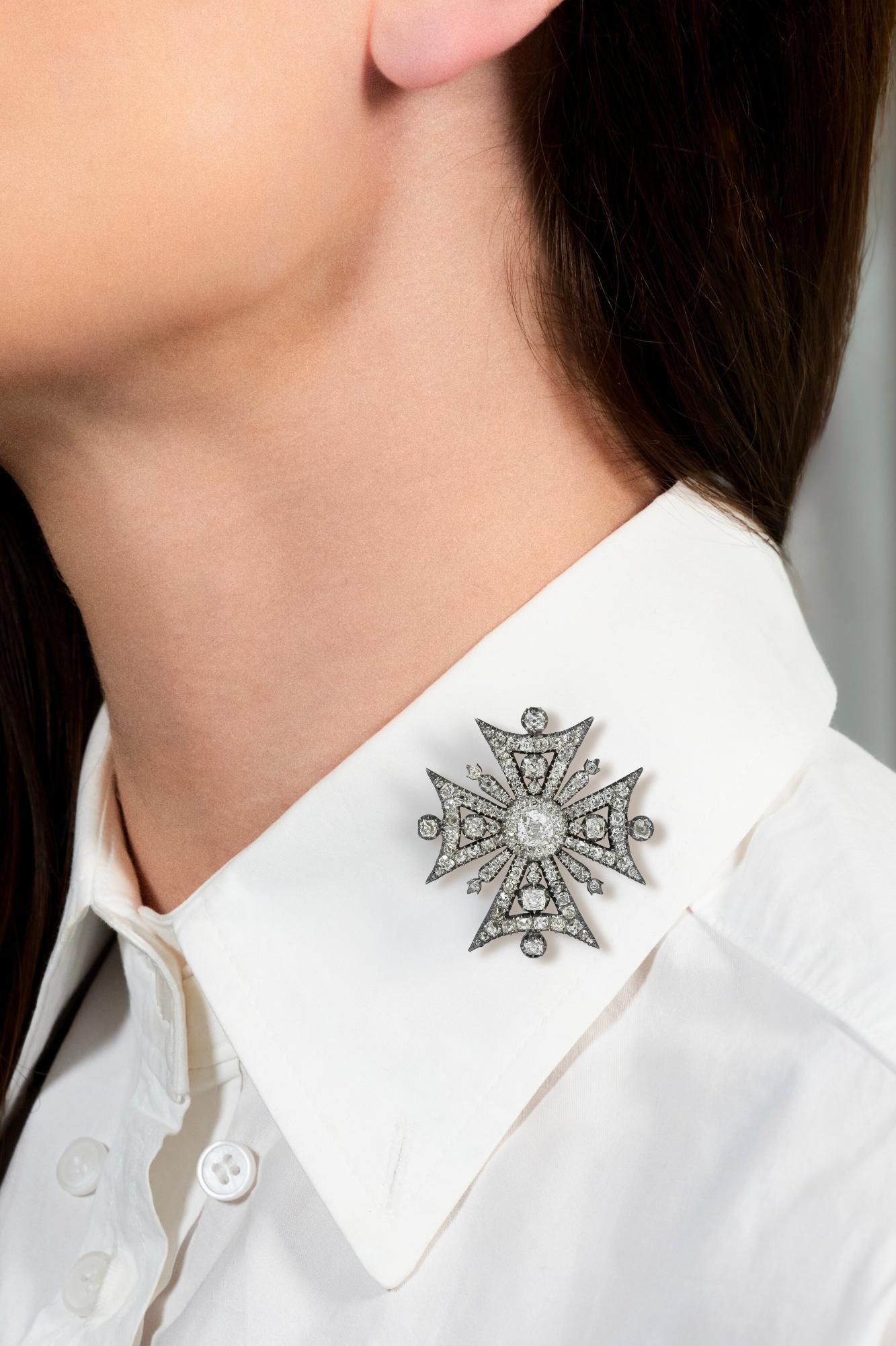 Designed as a silver-topped Maltese cross form suspending from a tapered bale
Centering an old mine cut diamond weighing approximately 0.89 carats
L color with VS2 clarity - prong set with a diamond halo surround
With additional old mine cut