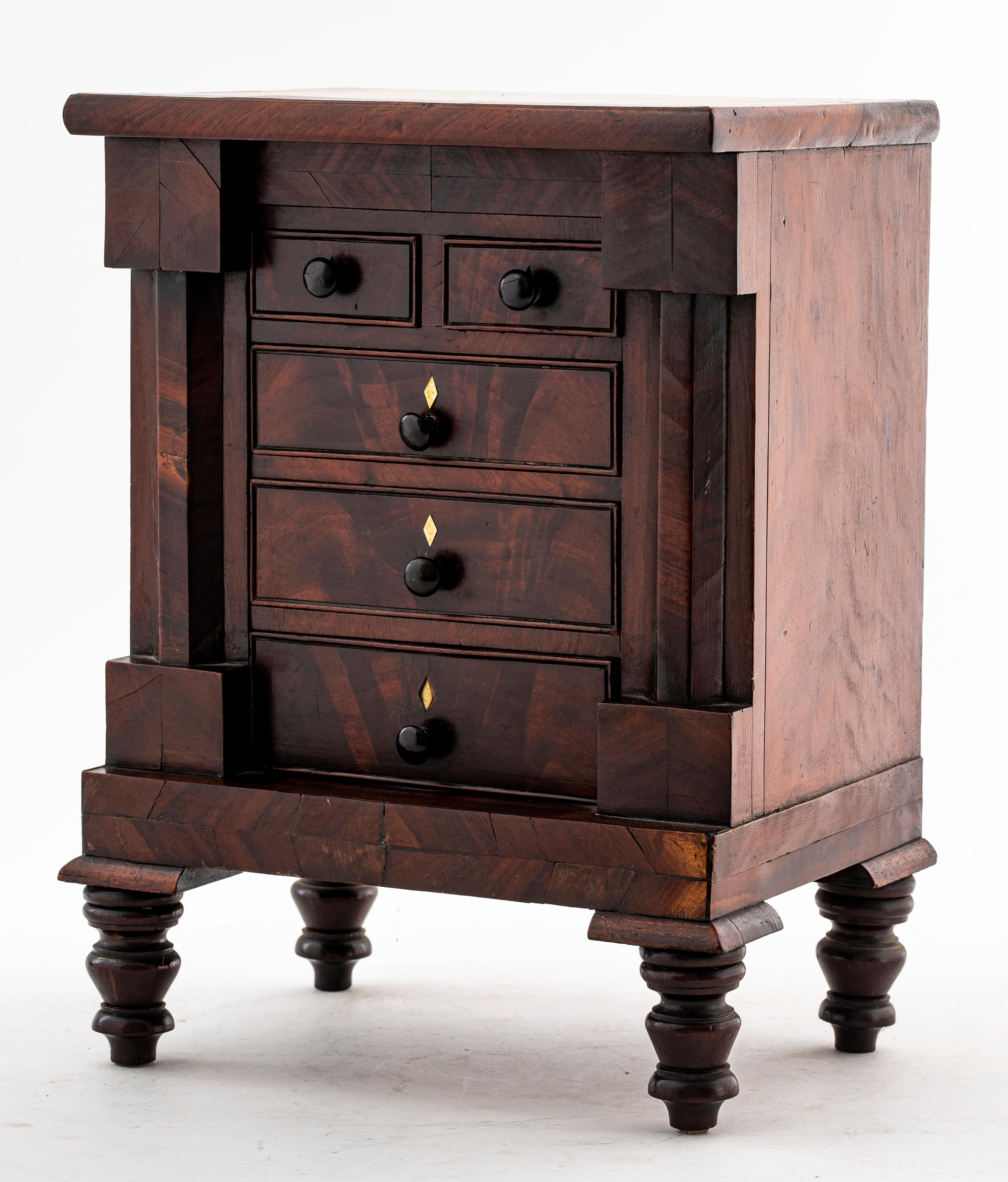 Victorian diminutive chest of drawers or jewelry chest in carved wood with turned legs, two short drawers above three large drawers, unmarked. Measures: 15.5