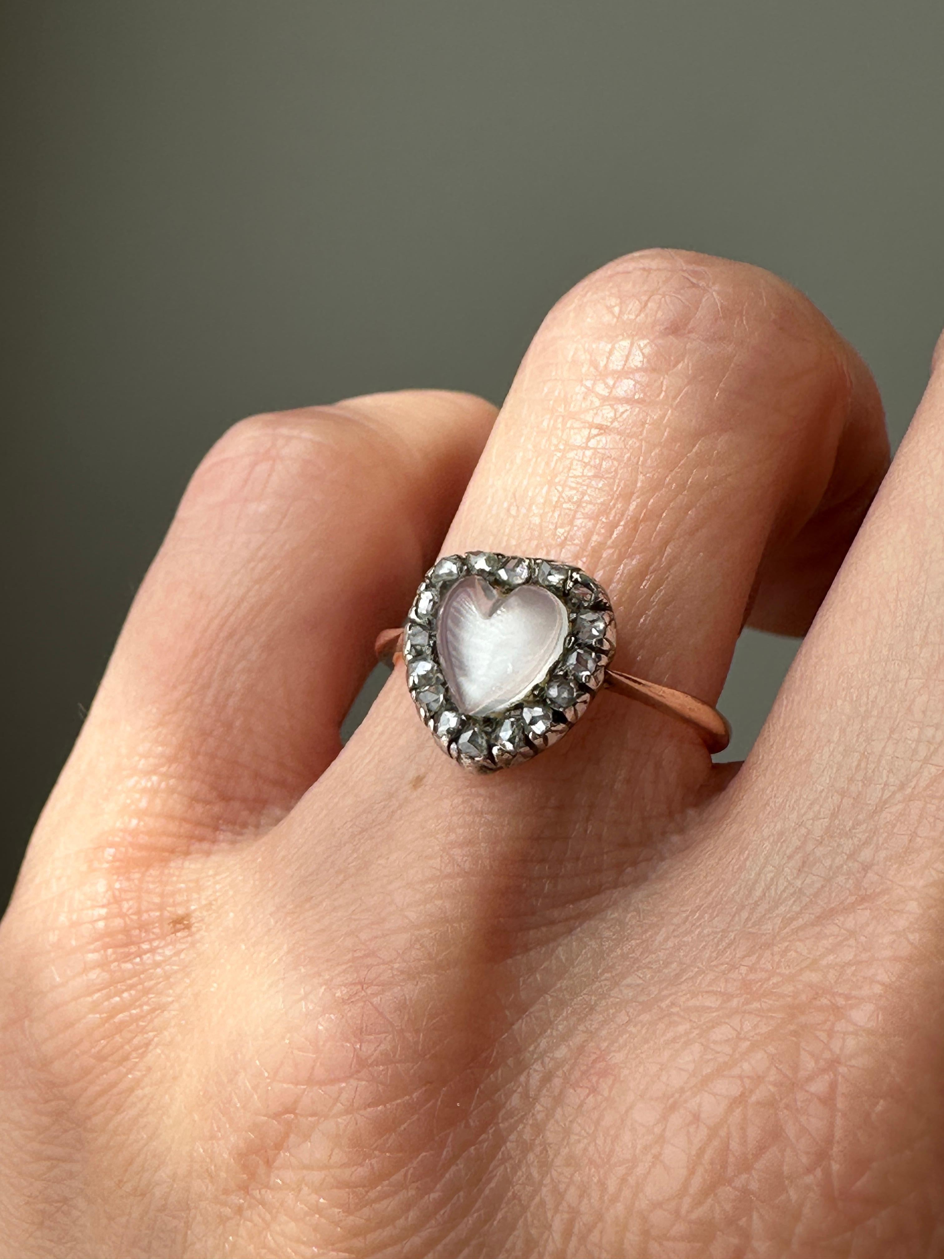 This romantic late Victorian/early Edwardian ring centers on a glowing heart-shaped cabochon moonstone outlined in glittering rose-cut diamonds. Hand fabricated in silver over 9K rose gold. English c 1890. Currently a ring size 5.75

