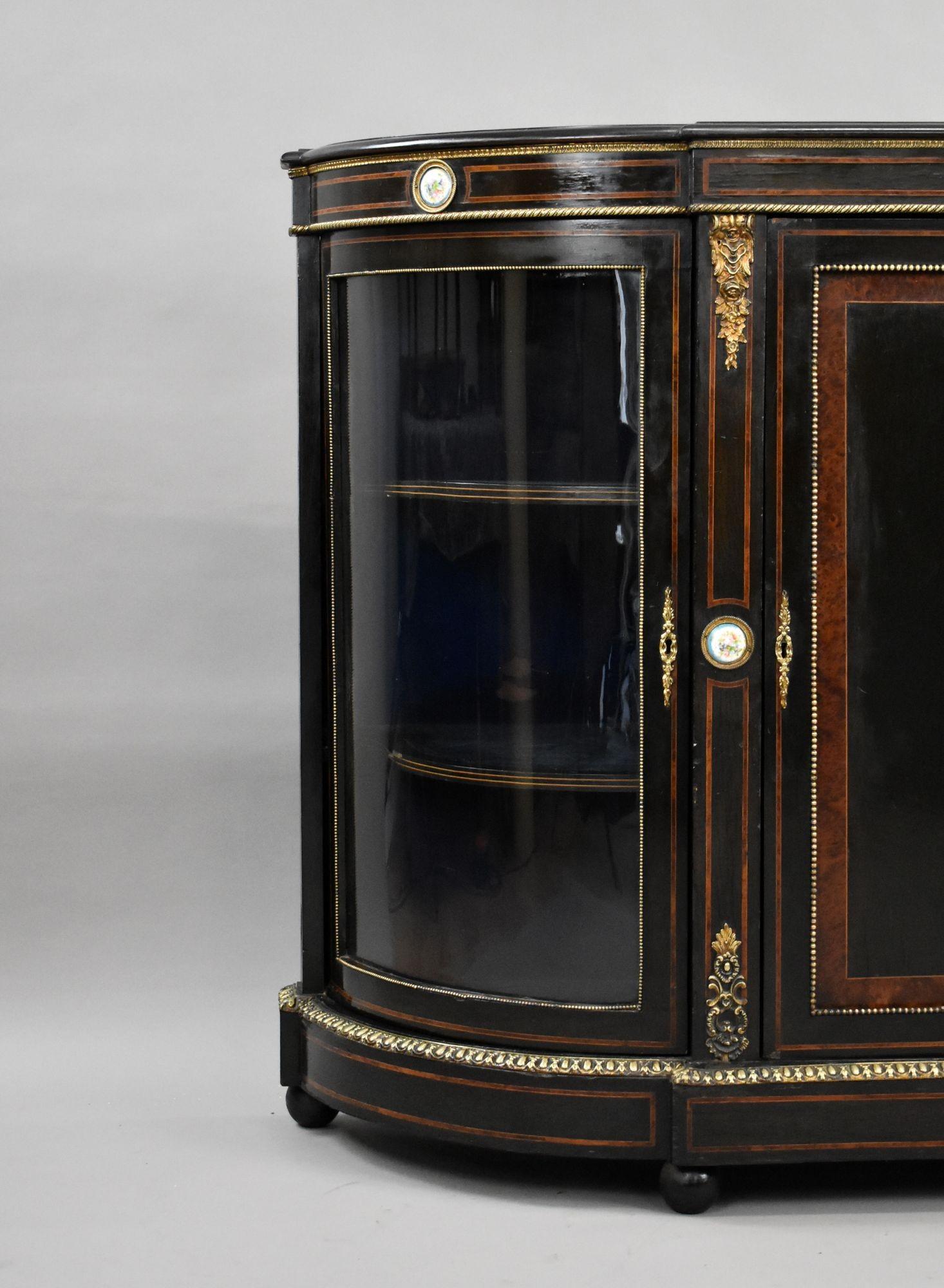 A late Victorian ebonised credenza, richly embellished with fine ormolu mounts and hand-painted porcelain plaques in the French Louis XVI style.
The shaped front features a central panel adorned with an oval Sevres-style porcelain plaque depicting a