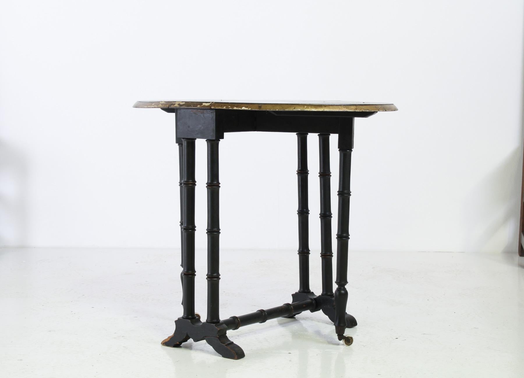 This elegant Victorian side table features a beautiful oval-shaped top with faux bamboo legs.  Made from hardwood with an ebonised black finish, one of the standout details is the worn, gilded edge around the table top, along with the worn patina