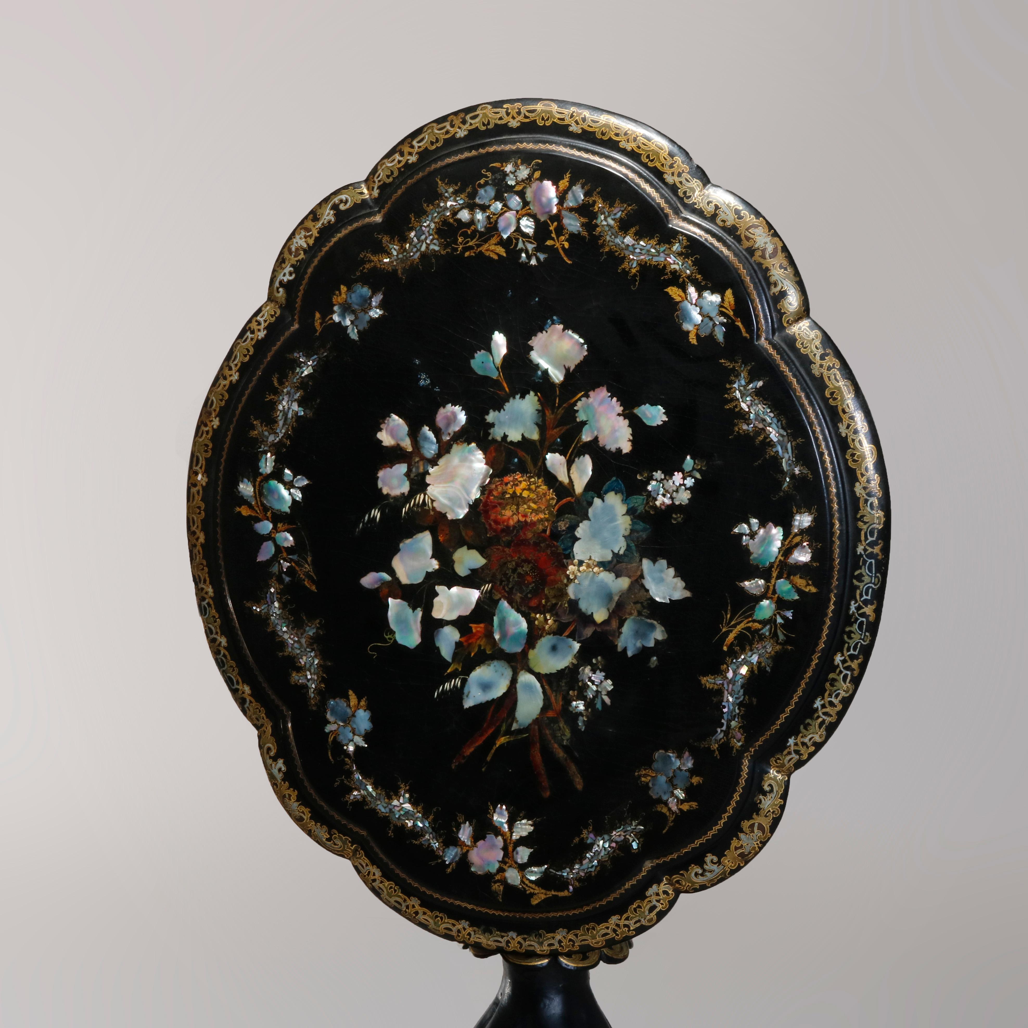 An antique Victorian tilt-top table offers Papier-mâché shaped top having mother of pearl inlay with hand painted and gilt decoration raised on turned column with melon form base with scalloped skirt seated on three feet, circa 1890

Measures: