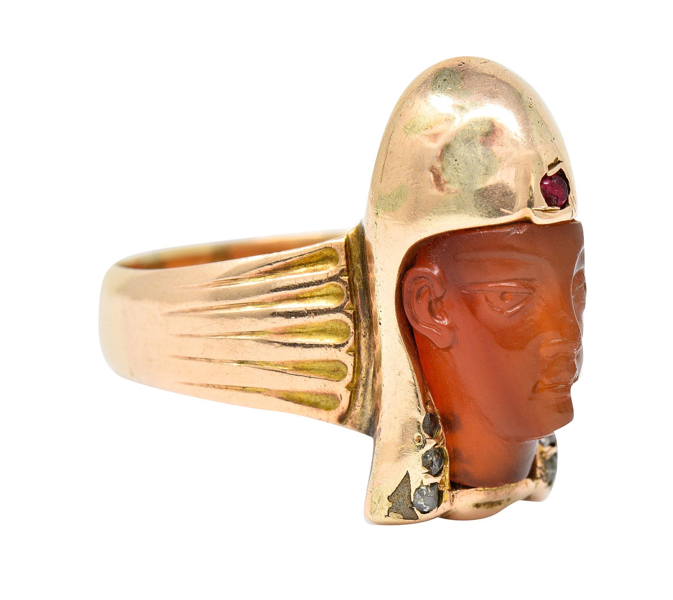Band ring is designed as an Egyptian Pharaoh carved from carnelian - translucent orangey red

Crowned in a gleaming gold headdress accented by rose cut diamonds and a round cut ruby

Completed by stylized and ribbed shoulders

Tested as 14 karat