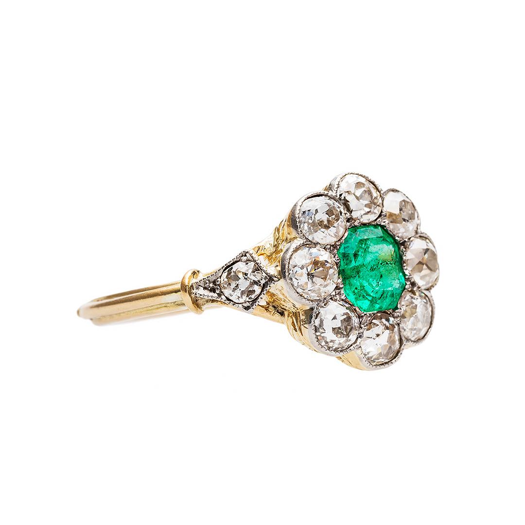 This is a delightful and authentic Victorian era (circa 1900) platinum and 18k yellow gold cluster ring with coveted French Hallmarks stamped into the outer shank. The ring centers a bright green natural emerald accompanied by a Guild Laboratory