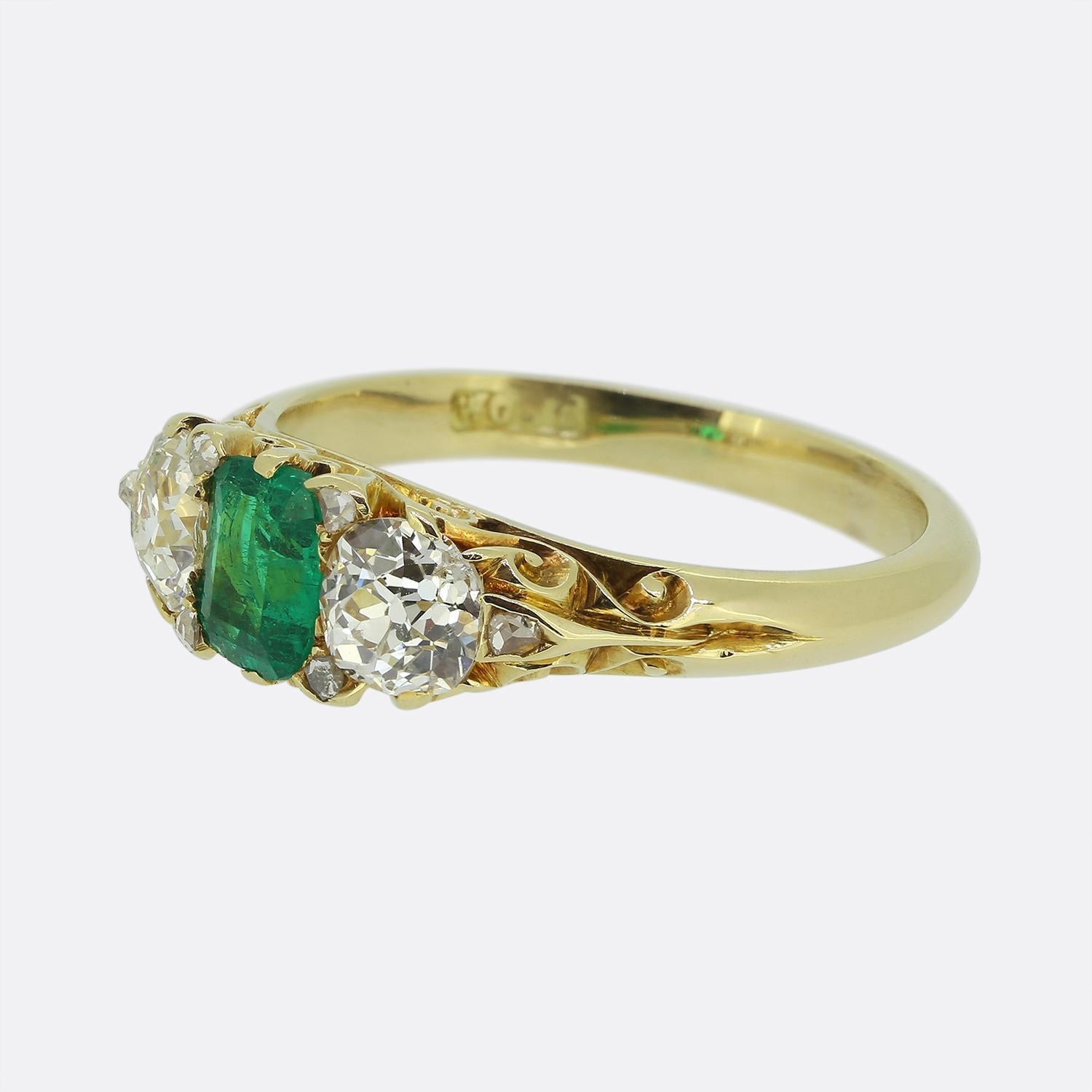 Here we have a delightful 18ct yellow gold three-stone ring dating back to the Victorian period. This antique piece features a captivating oval-faceted green emerald at its centre, flanked by two bright white round faceted old European-cut diamonds.