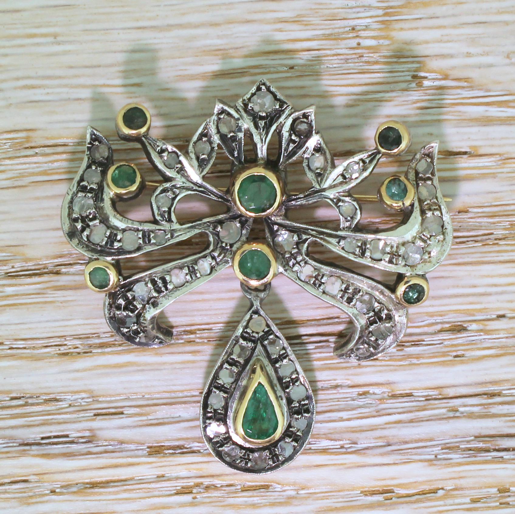 A dramatic Victorian brooch. This impressively designed piece features forty-five rose cut diamonds grain set in open back settings, with nine verdant green rubover-set emeralds, with an articulated pear drop at the bottom. This heavyweight brooch