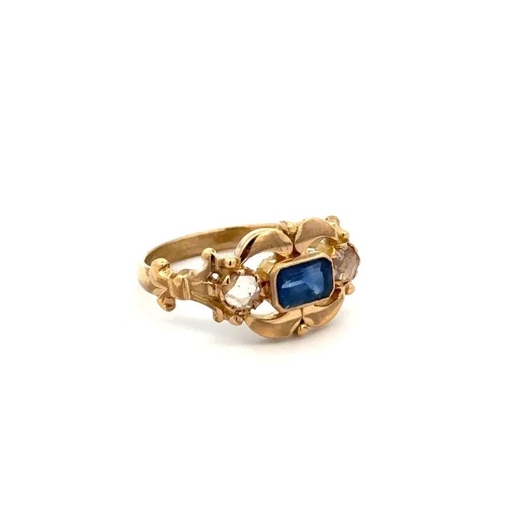Simply Beautiful! Finely detailed Emerald Cut Sapphire and Diamond Gold Ring. Centering a securely Hand set Emerald Cut Sapphire, weighing approx. 0.60 Carat, accented either side with Rose Cut Diamonds. Hand crafted 18K Yellow Gold mounting. Size