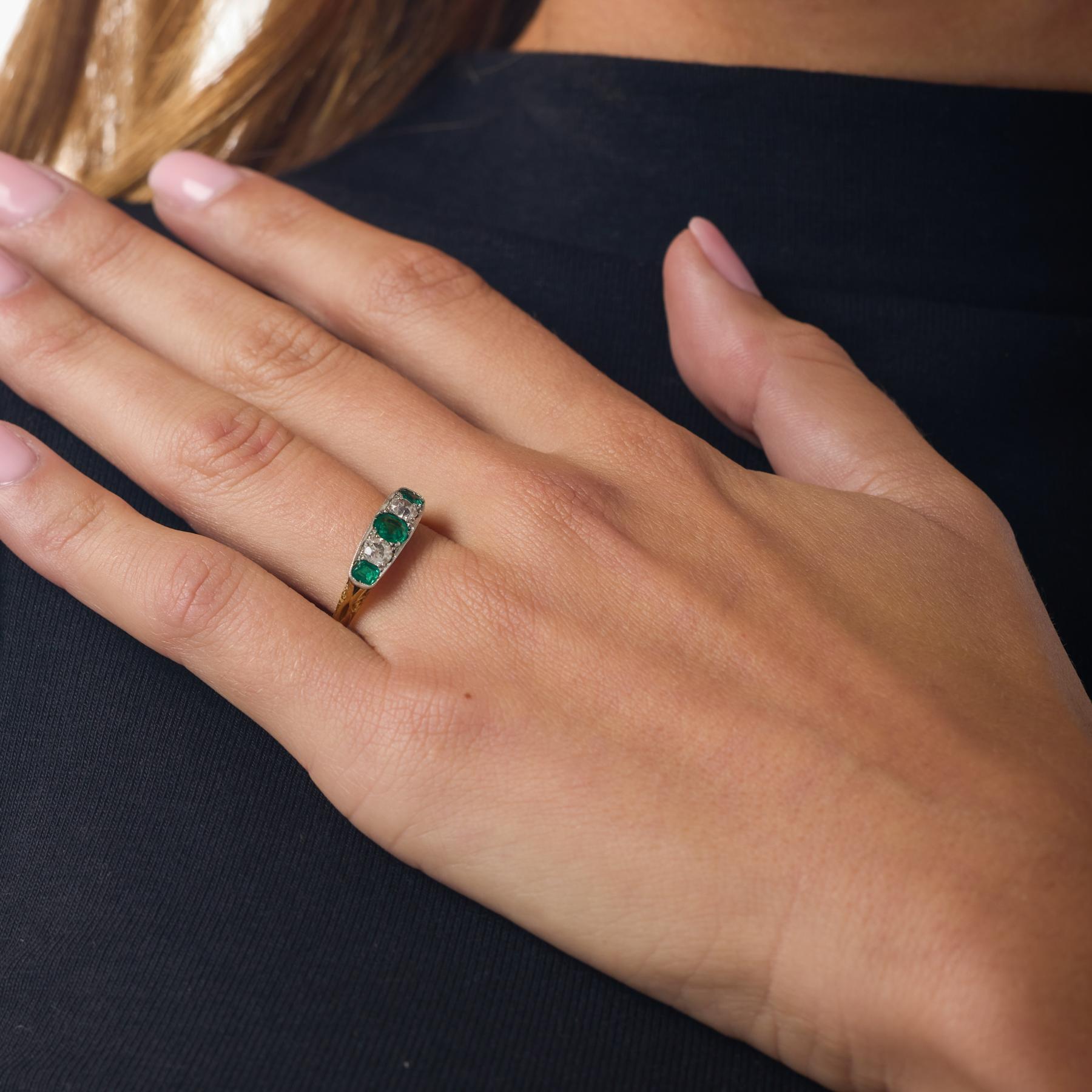 Cette bague victorienne à cinq pierres allie l'éclat vert luxuriant des émeraudes et le doux scintillement des diamants anciens, créant un mélange harmonieux de couleurs et de lumière qui semble à la fois historique et magnifiquement équilibré. Les