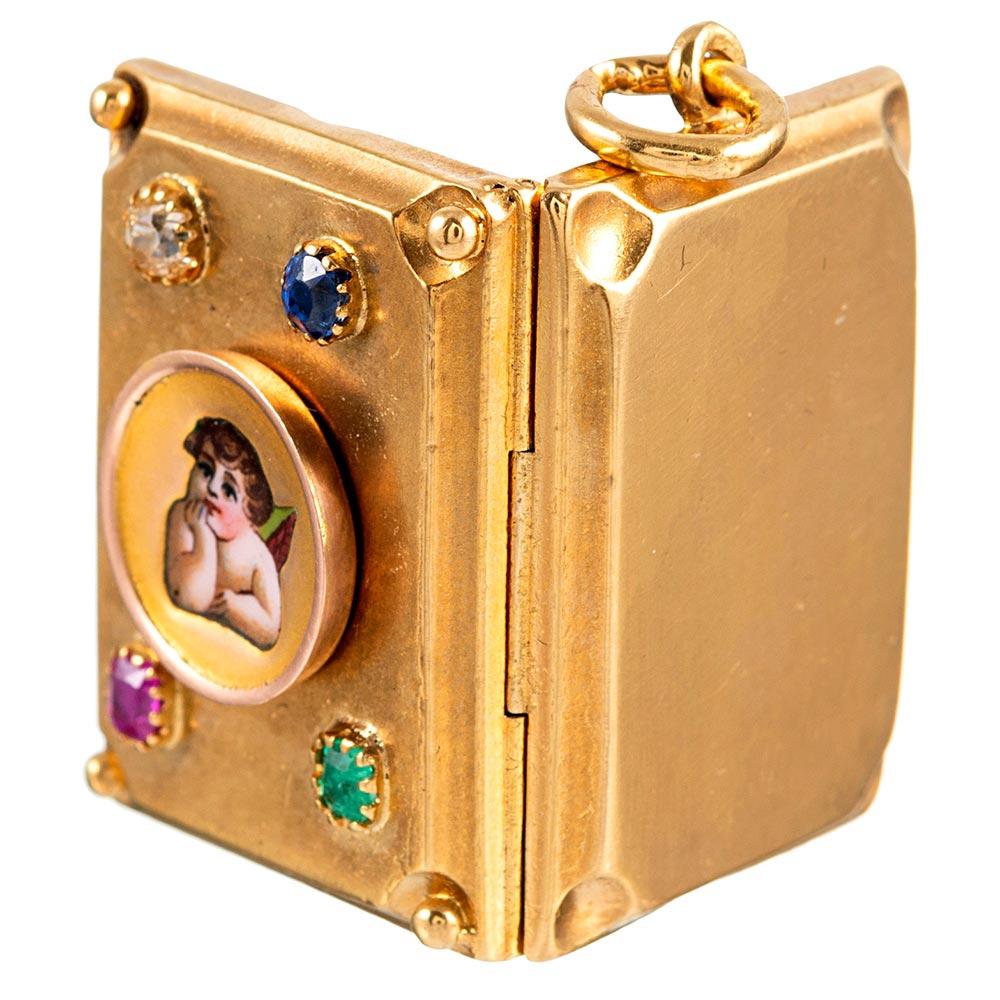 A charming rectangular locket, shaped like a book and opening in kind, this 18 karat yellow gold locket is decorated with an enamel cherub, with each corner speckled with a gemstone. One ruby, emerald, diamond and sapphire dots each corner, with a
