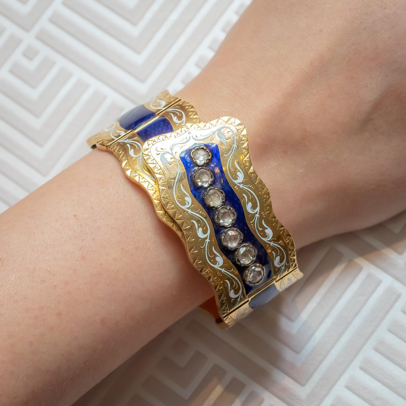 A Victorian enamel, diamond and gold bangle, formed of five plaques, with blue guilloche enamel centres, with scrolling white enamel decoration. The centre plaque is set with six rose-cut diamonds, each measuring an estimated 4.5mm in diameter, the
