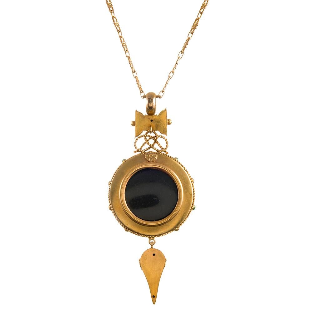 18k yellow gold sculptural pendant, almost Aztec in its rendering, but distinctly Etruscan in design, set in the center with a cabochon garnet and framed by crisp white enamel and green enamel dots at the “hour markers”. A stylized bow tie shaped