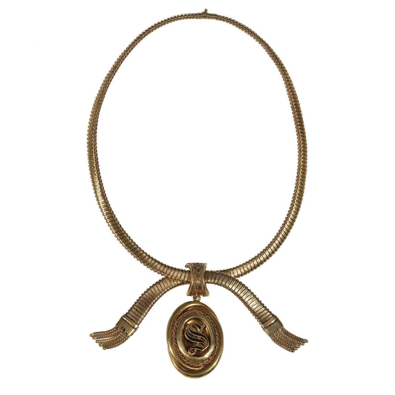 Of neglige design, the flexible collar of gaspipe linking terminating in two tassels at the front with a locket at the centre decorated with a S motif set with enamel

length 450mm approximately