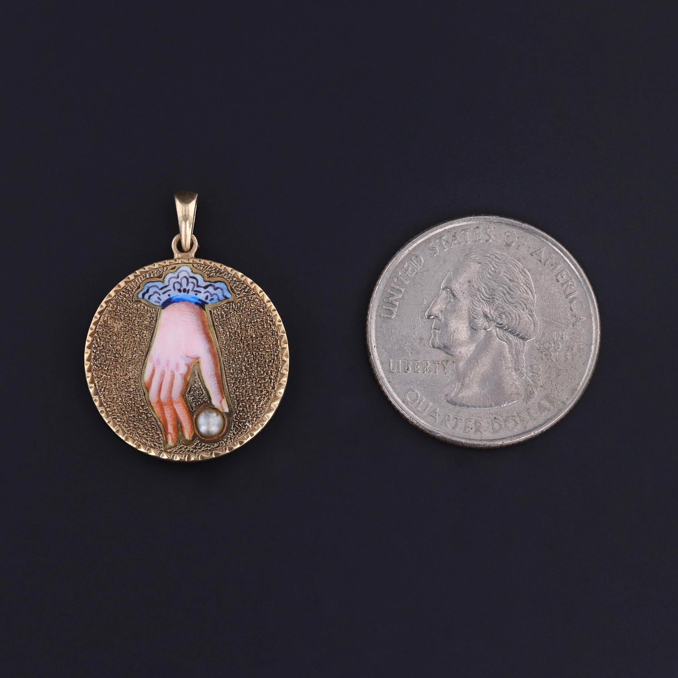 Un ciondolo in oro 14k con una mano smaltata che afferra una perla. È stato creato a partire da un bottone antico (circa 1870) che il nostro gioielliere ha trasformato aggiungendo un fondello e una coda in oro 14k.

Il pezzo misura 1,1 pollici dalla