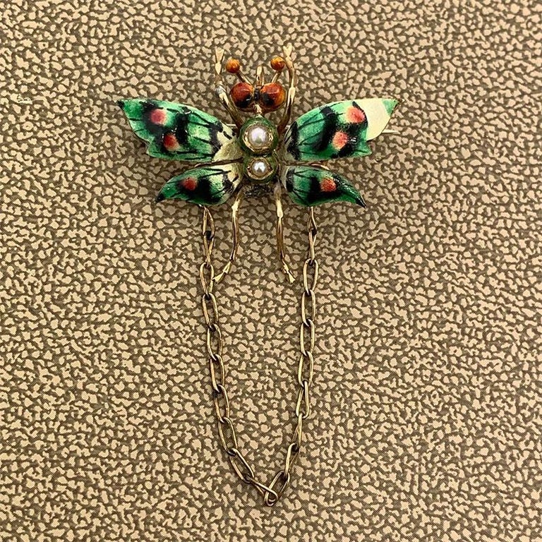 A Victorian butterfly brooch with vibrant hand painted enamel and seed pearls for the body. This 14K yellow gold brooch is accompanied by a chain and a loop for it doubling as a pendant.

Brooch Length: 0.95 inches

Brooch Width: 1.15 inches