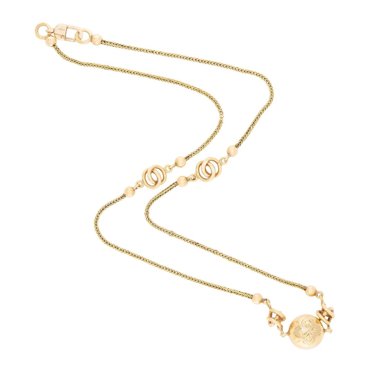 A stunning and intricate necklace from the Victorian (ca1880s) era! Crafted in 18k yellow gold, this necklace features a central, three-dimensional ball charm. The surface of the ball is decorated with intricate etchings, which add to the unique