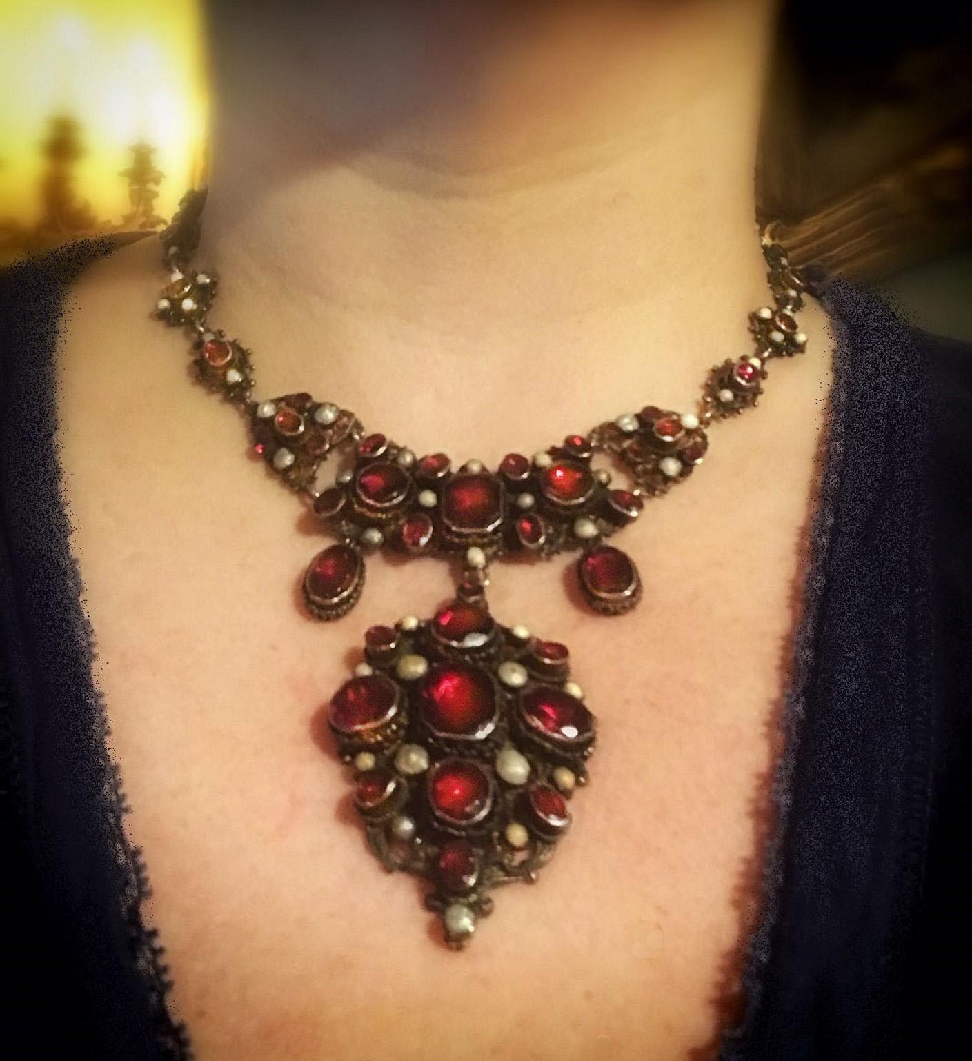 This regal necklace features 47 cut and polished deep red garnets. The entire bib is worked in silver gilt. Each linked piece is topped with a glowing bevel set garnet all the way around the neckline and several more garnets as it draws into the