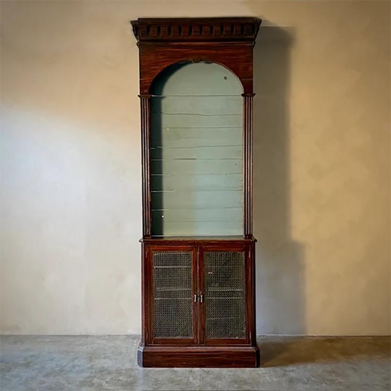 Questa libreria o credenza dipinta della fine del XIX secolo, proveniente dall'Inghilterra, offre un'accattivante miscela di funzionalità ed estetica ornata. La parte superiore presenta uno spazio espositivo ad arco con uno sfondo intarsiato, ideale