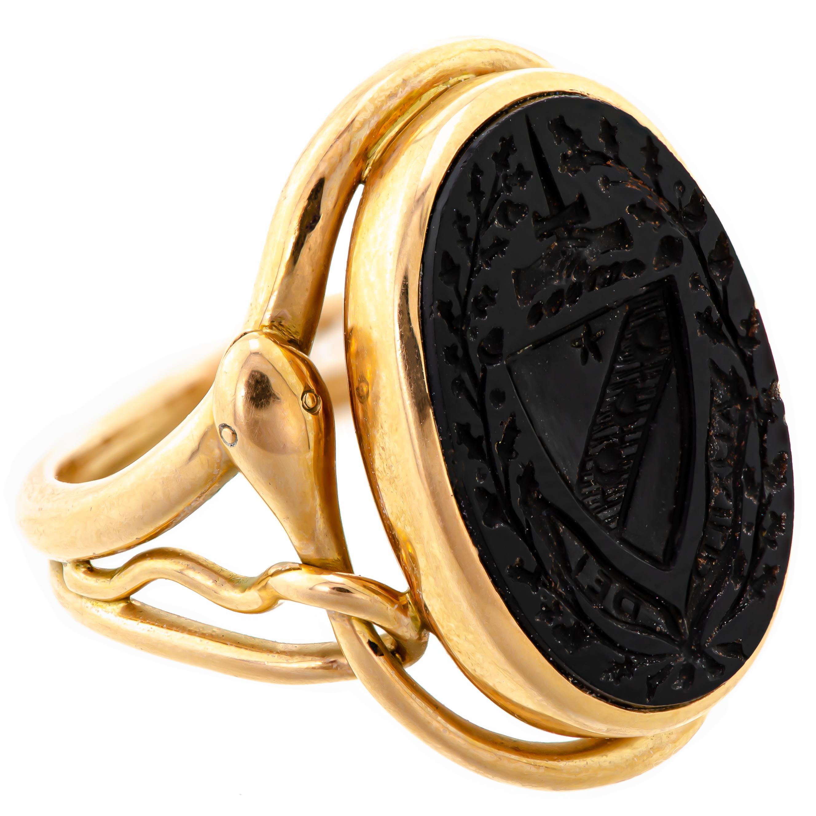 Pause to marvel at the exceptional craftsmanship of this English Victorian Signet Intaglio Crest Signet and 15Kt Yellow Gold Snake Ring! The ring boasts an oval family crest shield and foliate design, meticulously carved from hardstone, measuring