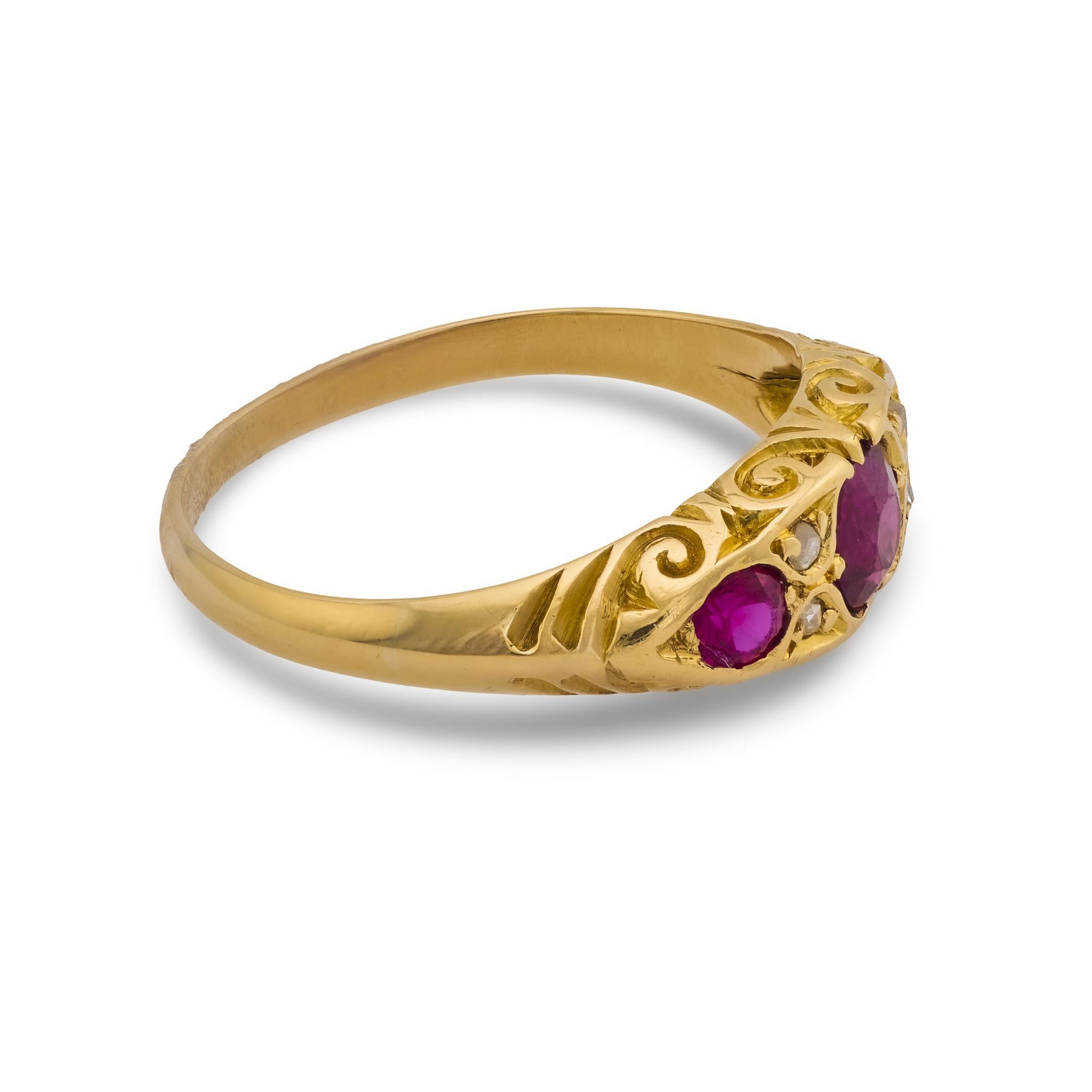Cette élégante bague victorienne met en valeur trois rubis vibrants de taille coussin encadrés par de délicats diamants de taille rose, le tout serti dans un riche or jaune 18k pour une allure antique intemporelle.