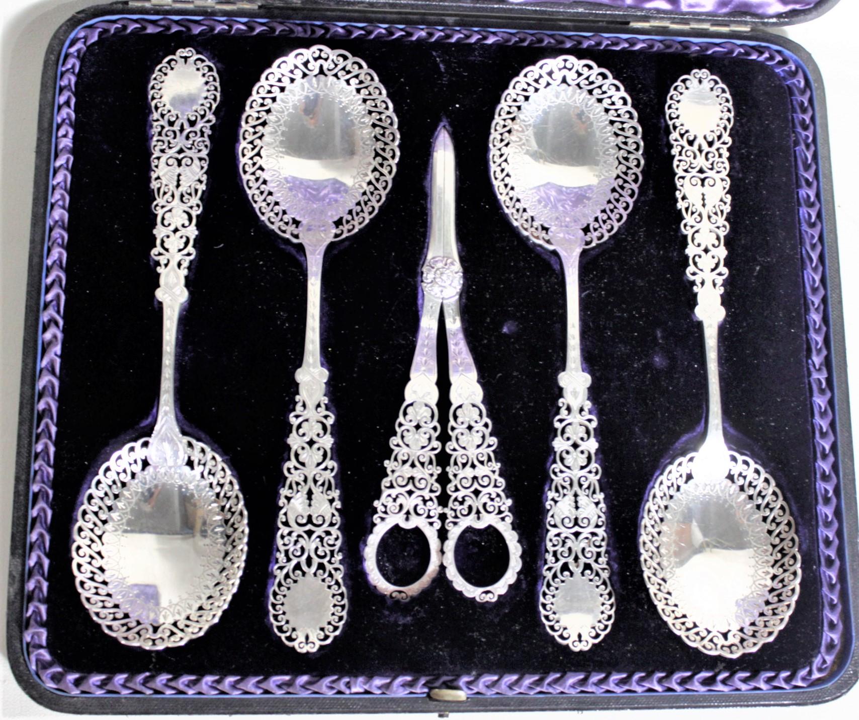 This antique sterling silver berry set was made in London England in circa 1880 in the period Victorian style. The set is composed of four large matching berry spoons and a pair of grape shears in a velvet lined fitted leather case. These sterling