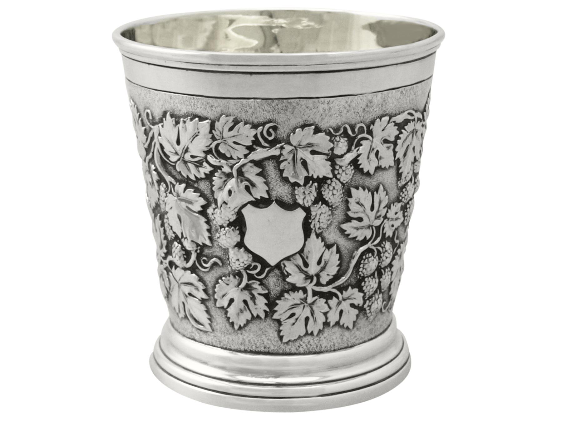 This fine antique sterling silver christening mug has a cylindrical tapering form onto a plain spreading collet style foot.

The body of this Victorian mug is ornamented with a fine and impressive chased decorated grape and vine decoration on a