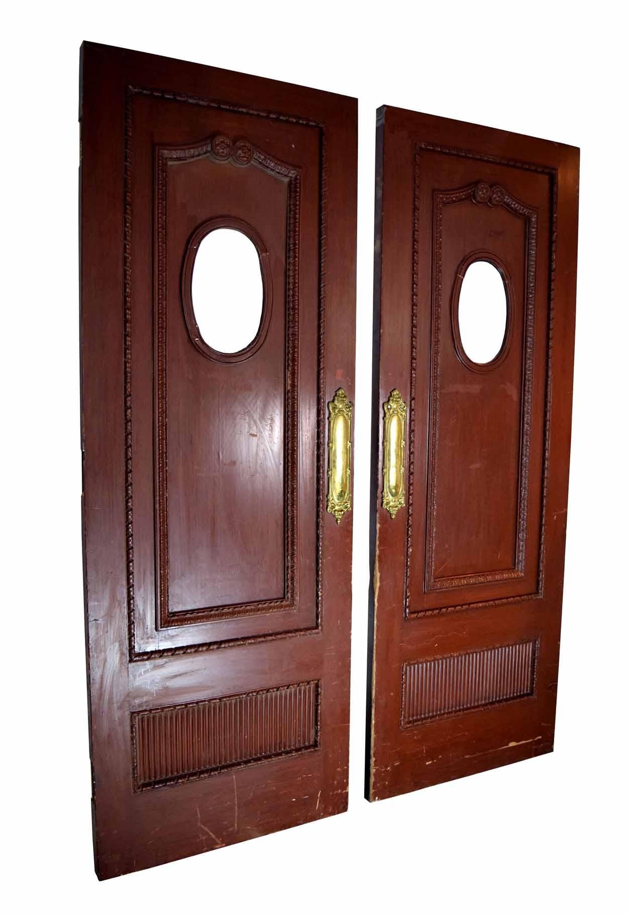 These Victorian double doors feature intricately carved details that add charm and visual interest. The details are reminiscent of nature, with floral carvings above the oval windows, and leaf-like carvings creating panels within the doors. These