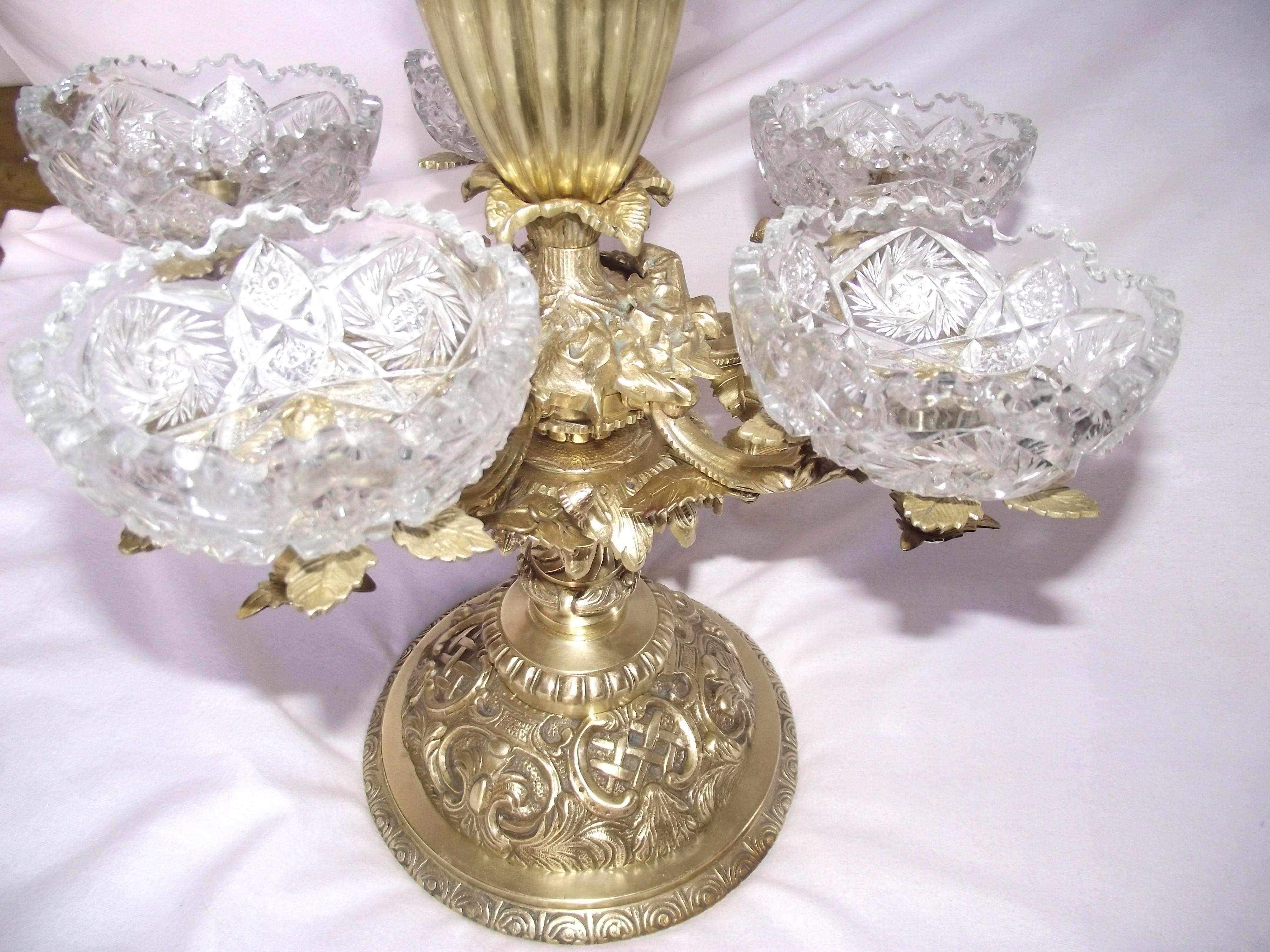 This elegant Victorian Eperne or centrepiece is made of very heavy solid brass. It has a thick large centre glass bowl which is surrounded by five matching saw tooth edged smaller bowls. This highly decorated piece is freshly polished and lacquered